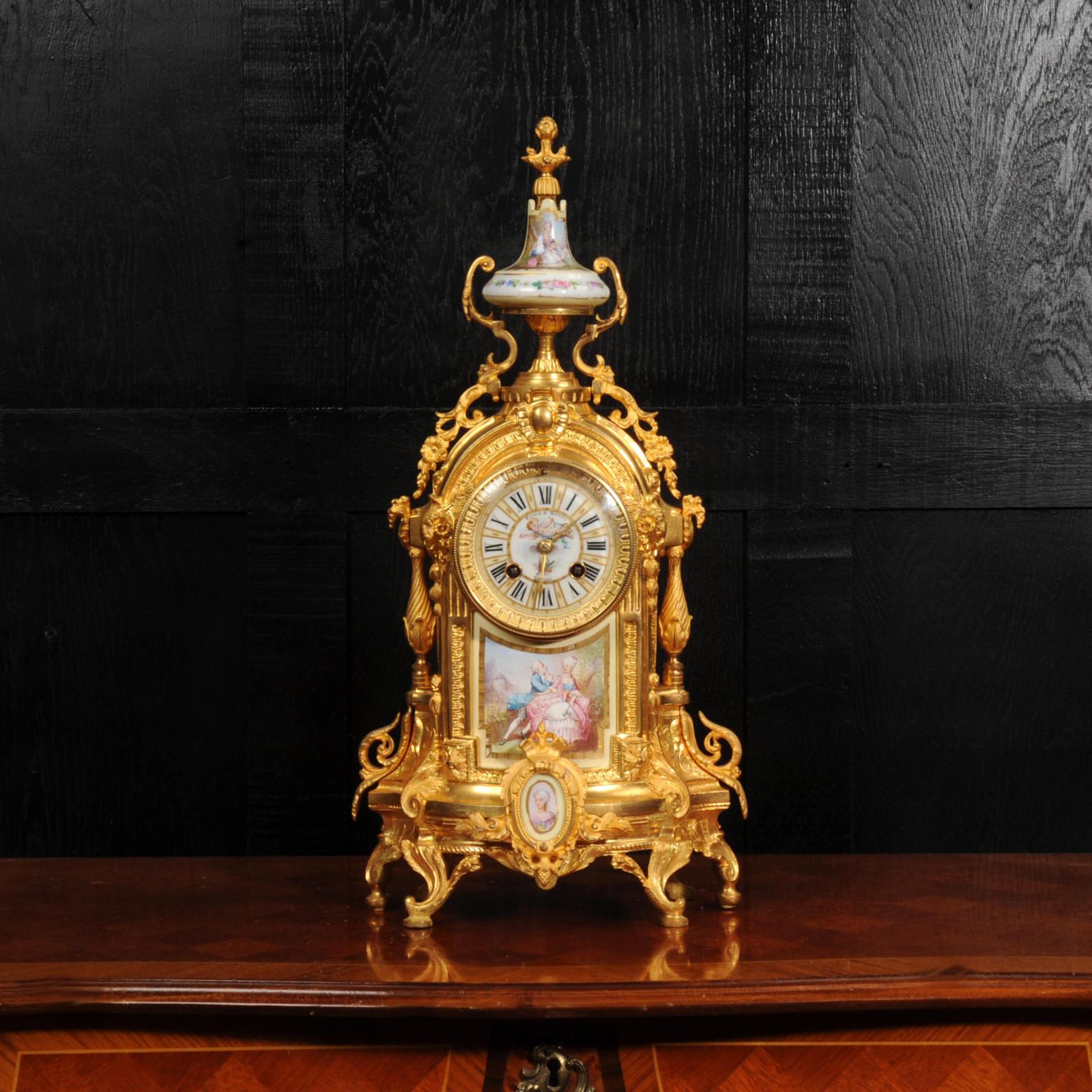 A richly decorative French mantel clock, finely modelled in gilt bronze and mounted with exquisite Sèvres style porcelain with a cream ground. The central porcelain panel depicts an elegantly attired couple in 18th-century dress, seated in a