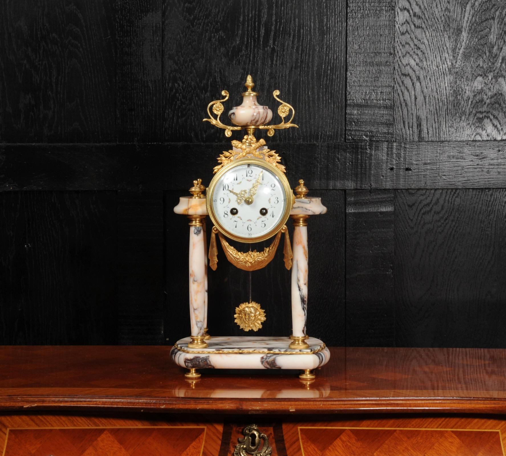 A stunning antique French portico clock, beautifully modelled in a stunning variegated specimen marble with salmon pink and silver grey veining. It is mounted with finely finished ormolu (gilded bronze) that is in excellent condition. The clock is