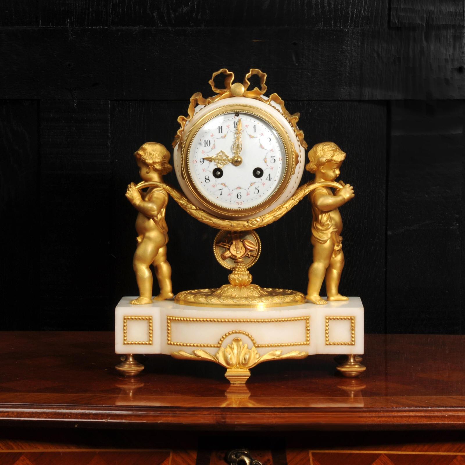 Une belle horloge française ancienne, de style Louis XVI, avec deux charmants chérubins portant l'horloge sur des couronnes de laurier. Le pendule avec des motifs musicaux appliqués, se balançant doucement en dessous. Il est magnifique, réalisé en