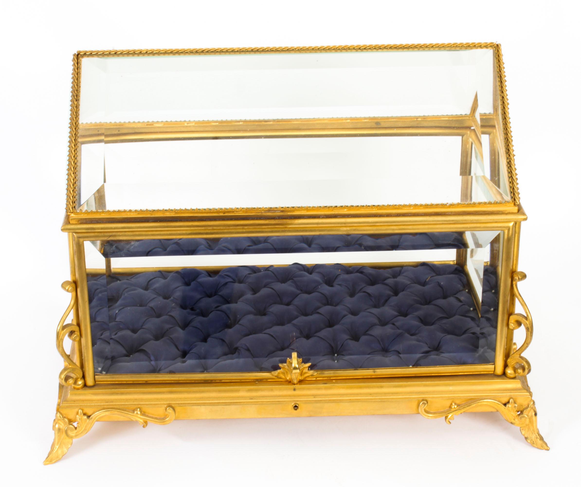 This is an elegant antique French ormolu and bevelled glass table top bijouterie cabinet, circa 1880 in date.
 
It is of Neo-Grec style and of rectangular form with hipped top and pull up door which opens to real blue silk padded interior.
