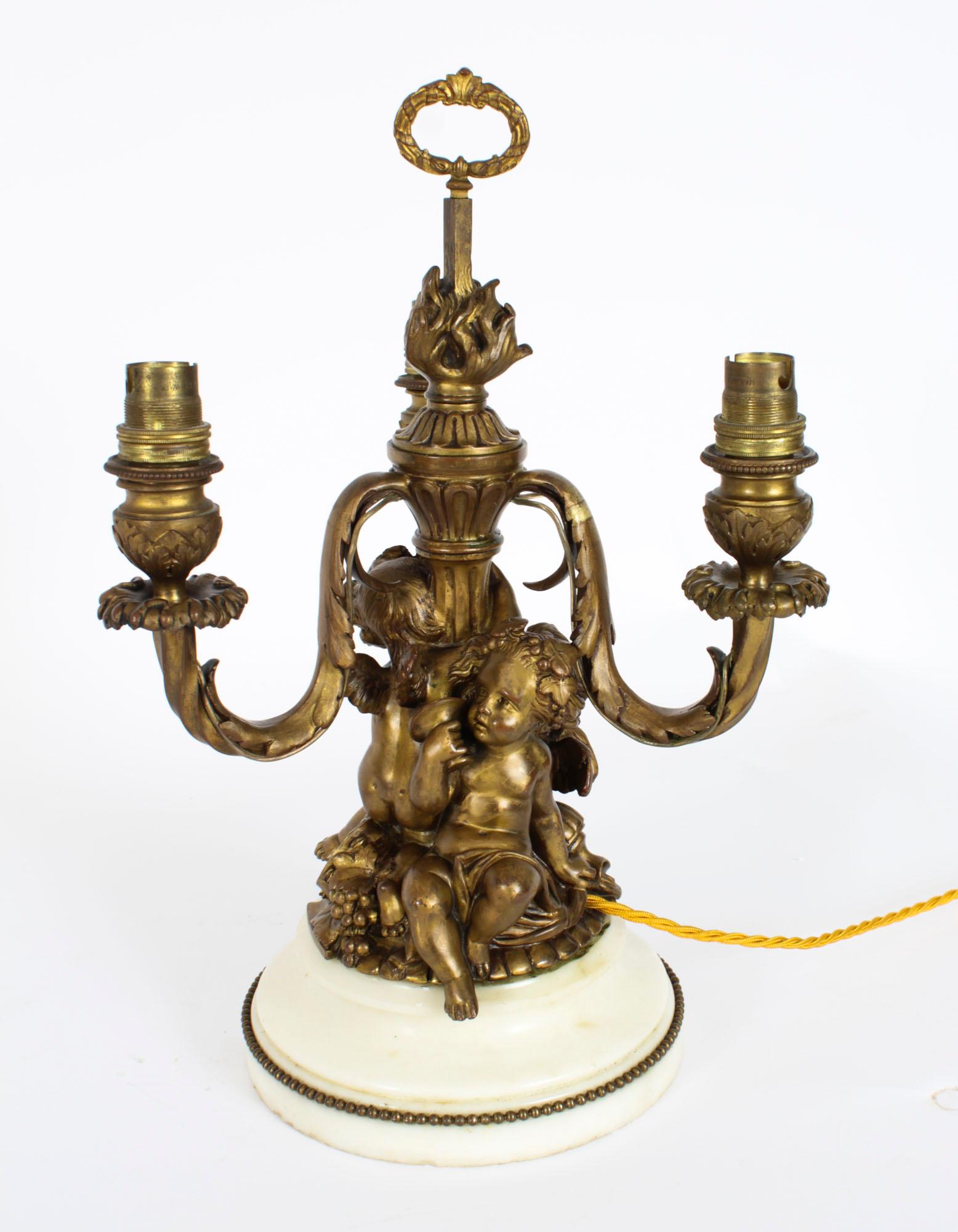 Il s'agit d'une lampe de table en bronze doré de style Louis XVI avec une base en marbre de Carrare, datant d'environ 1870.
 
Candélabre en bronze doré à trois branches, transformé plus tard en lampe de table, avec trois chérubins ailés reposant sur
