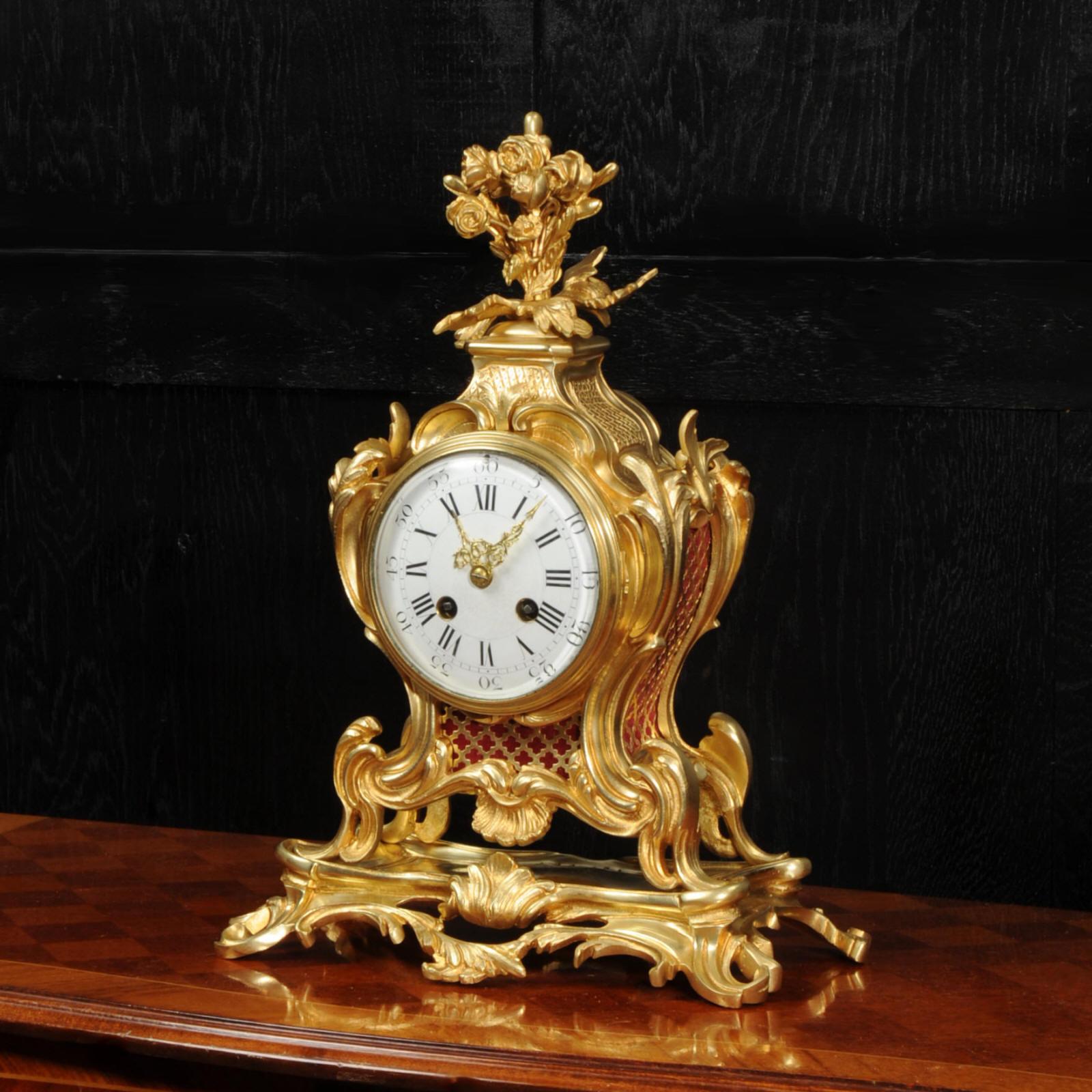 A stunning original antique French Rococo clock. It is beautifully sculptured with finely finished scrolls, curves and acanthus leaves in finely gilded bronze. Panels backed with red fabric lighten the design. The reflection of pendulum can be seen
