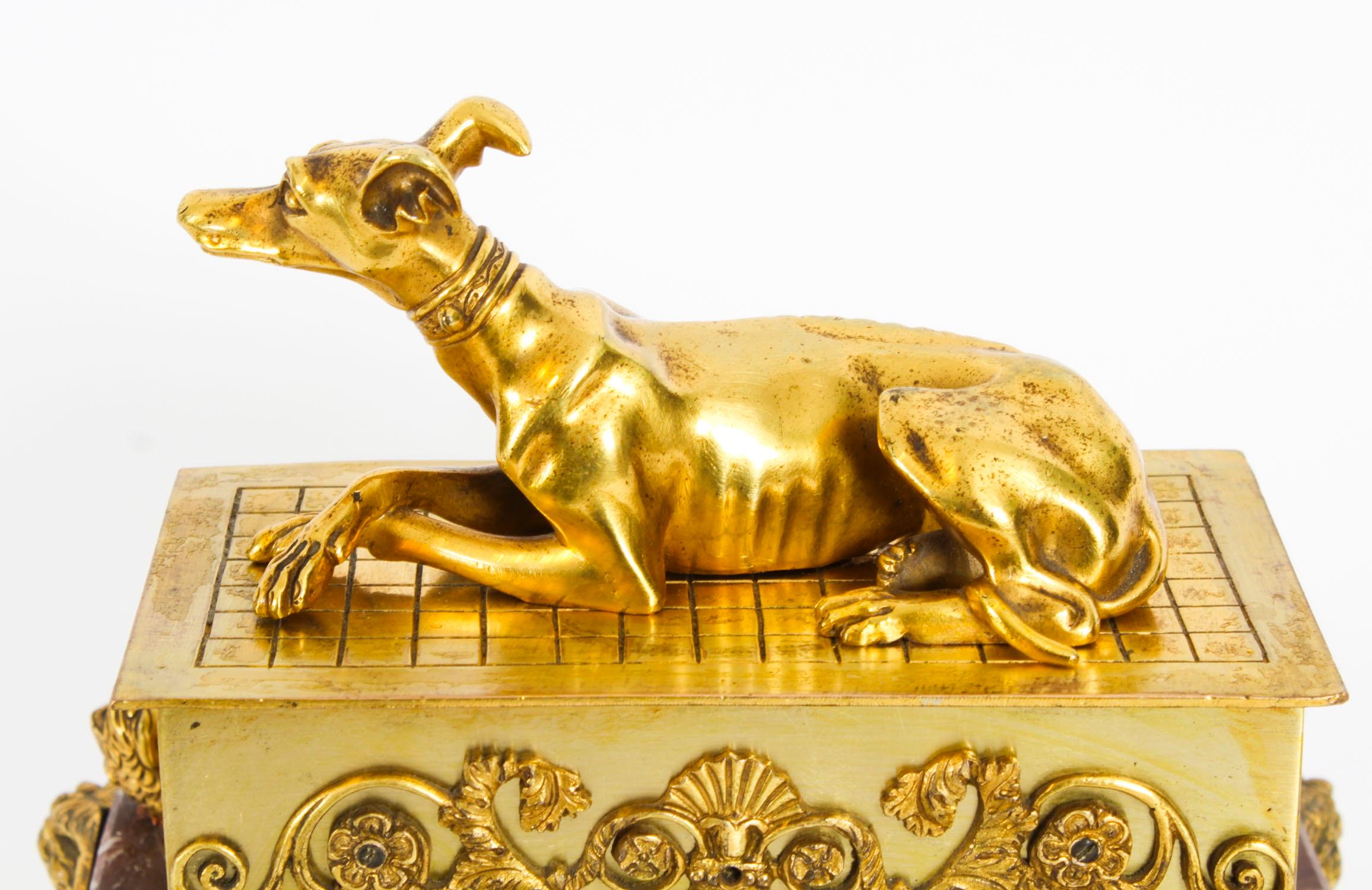 This is a fine antique French Empire Revival ormolu and patinated marble casket, circa 1820 in date.

Of rectangular form decorated with  a central sculpture of a reclining grey hound on the lid of the casket, which lifts off to reveal a casket with
