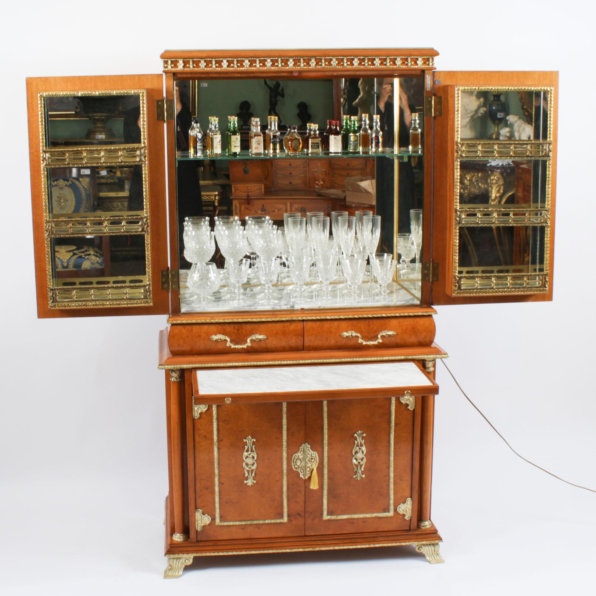 Il s'agit d'un superbe cabinet de cocktail en ronce de noyer et bronze doré, avec un intérieur en miroir, de la plus haute qualité, accompagné d'une série de verres en cristal taillé,  datant d'environ 1930.

Les portes s'ouvrent pour révéler un