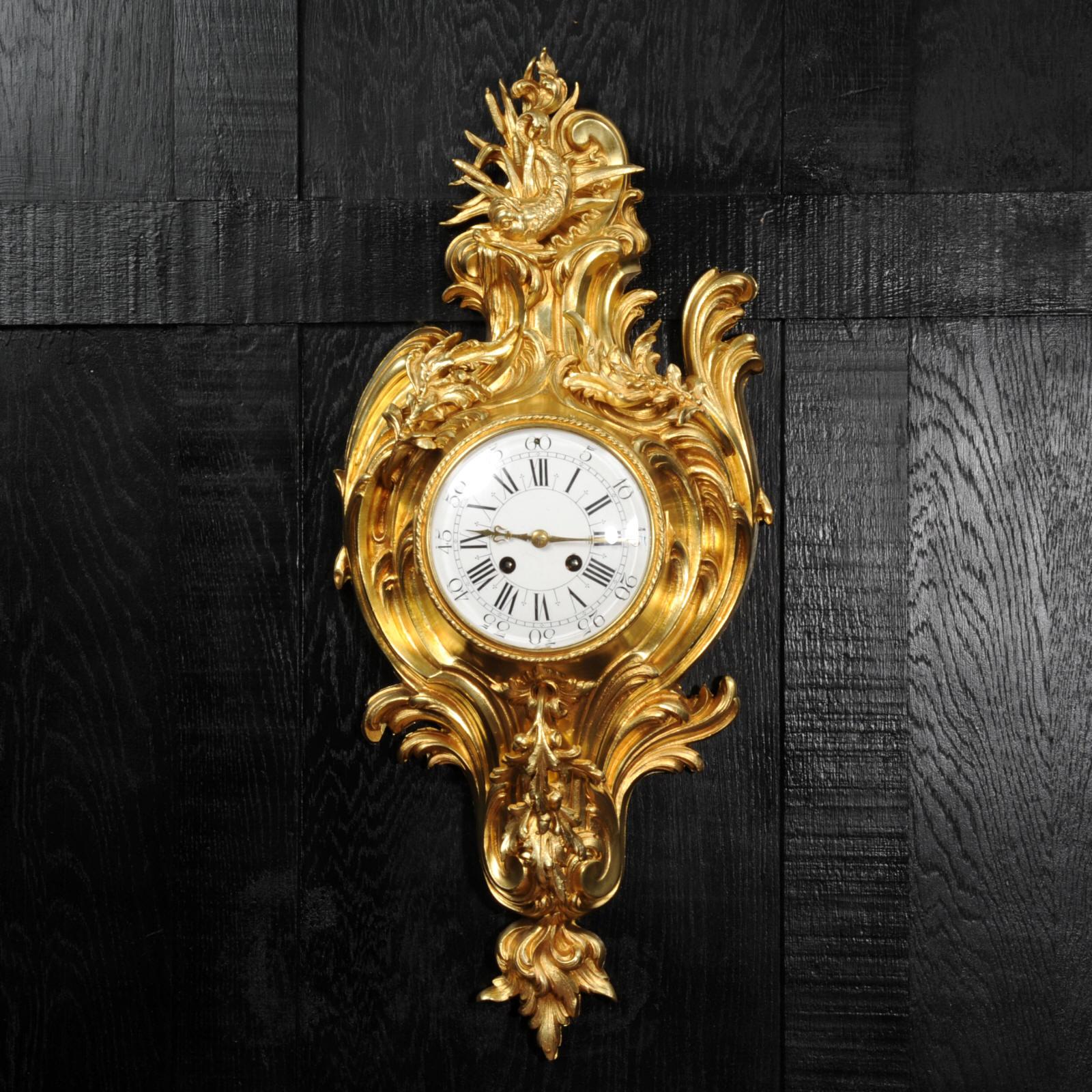 A beautiful original antique French cartel wall clock, circa 1880. It is finely made in ormolu (finely gilded bronze doré) in the Rococo style and features a dolphin to the top, riding a C scroll of surf. The case is formed of flowing splashes of
