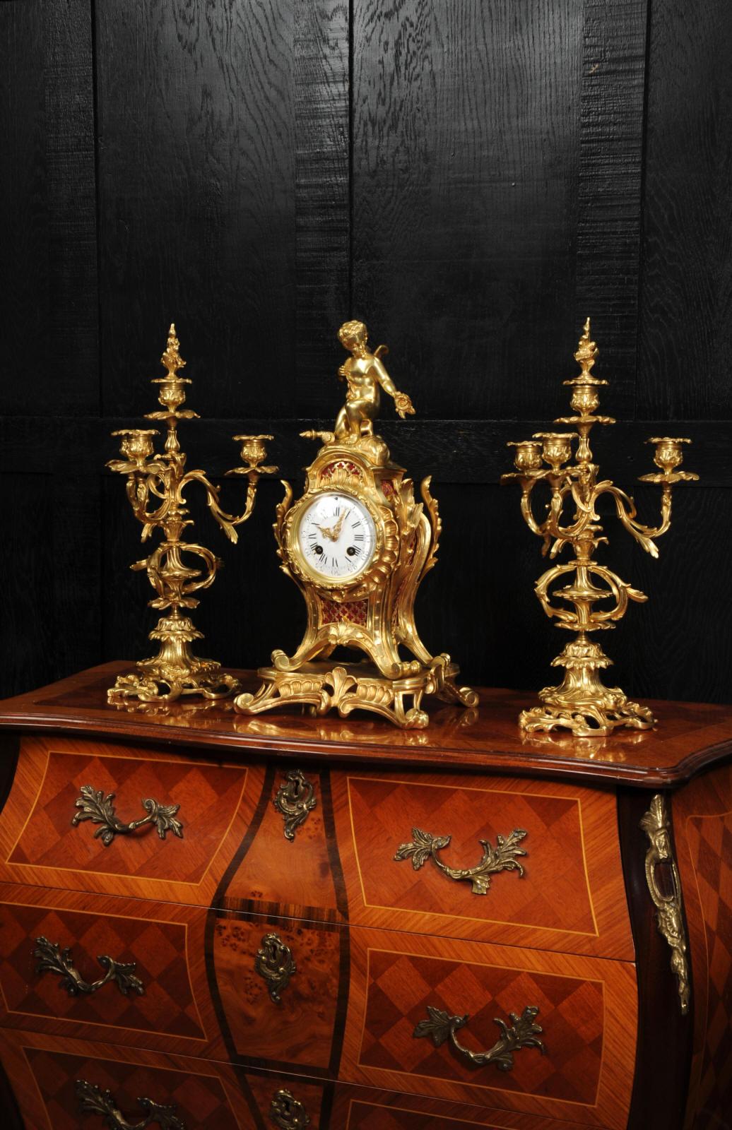 A beautiful antique French ormolu clock set in the Rococo style. It features cupid as a cherub, seated to the top with torch and quiver of arrows, offering a posy of flowers. The case made of finely gilded bronze in the Louis XV style of bold