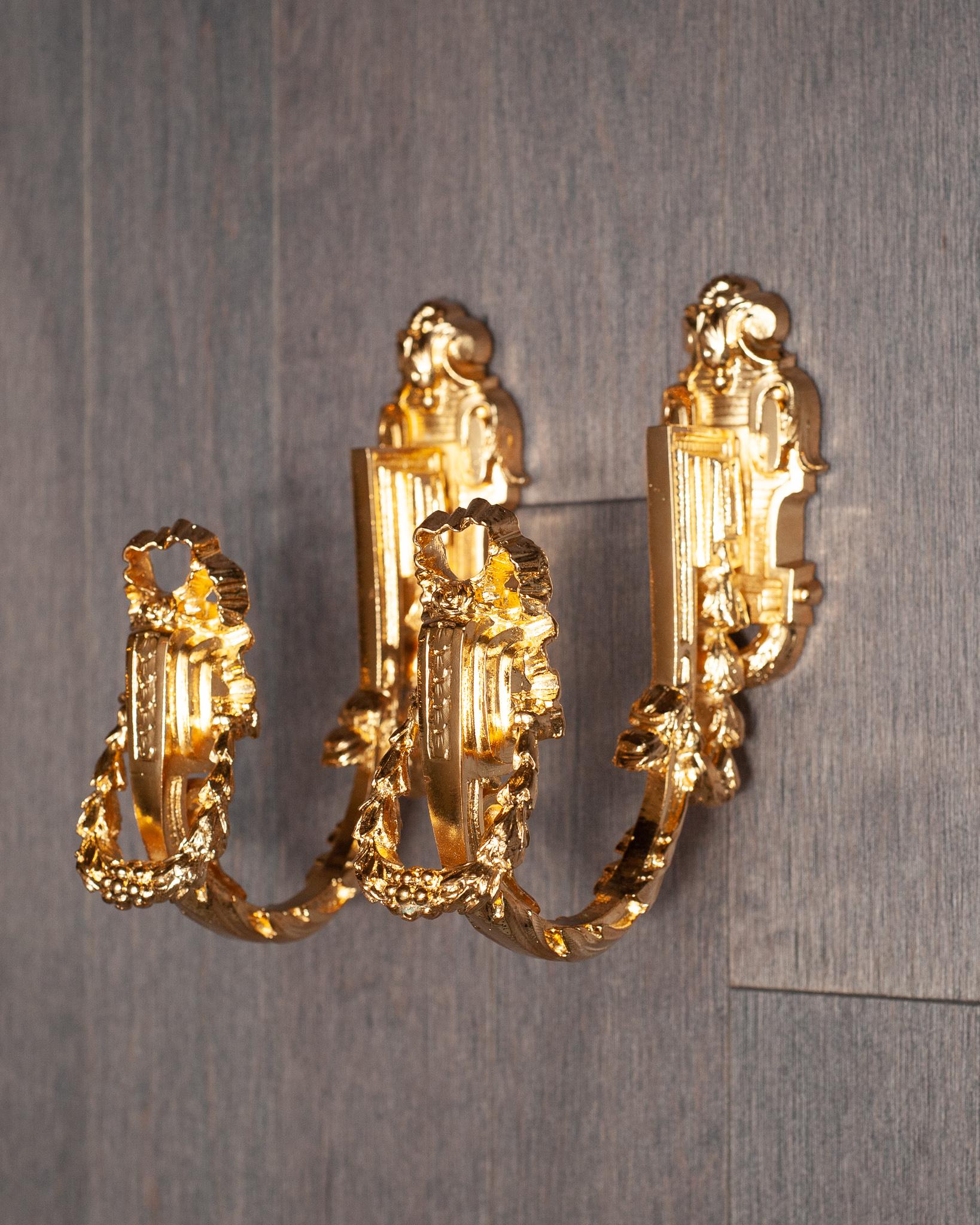 An antique French pair of sculpted gilt bronze curtain hooks or tie-backs richly decorated with foliage and garlands.