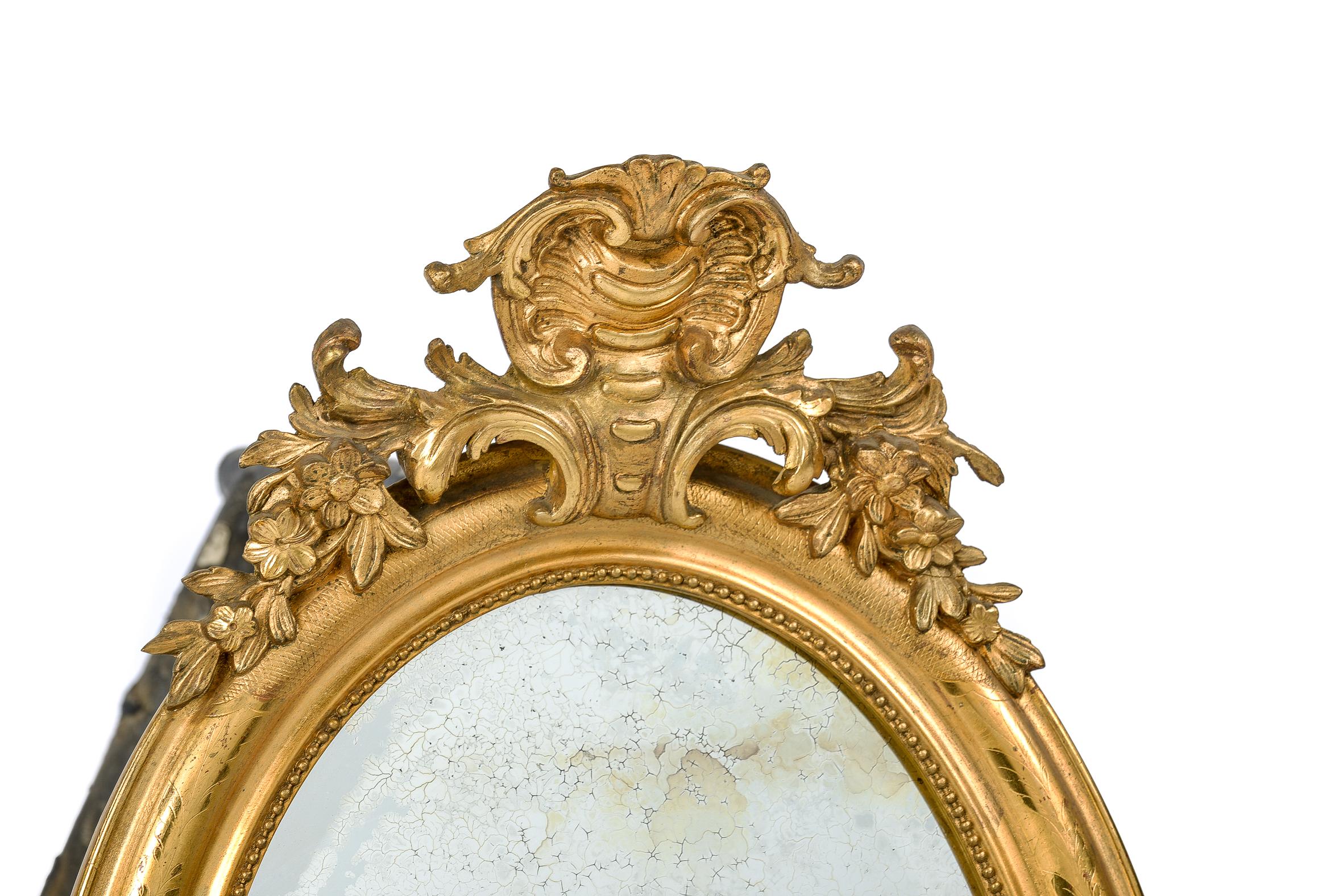 A beautiful antique French oval mirror with handsome ornaments. The top ornament is centered upon a shell pediment flanked by acanthus and floral elements. The lower ornament has the same design elements and is smaller of size. The most elevated
