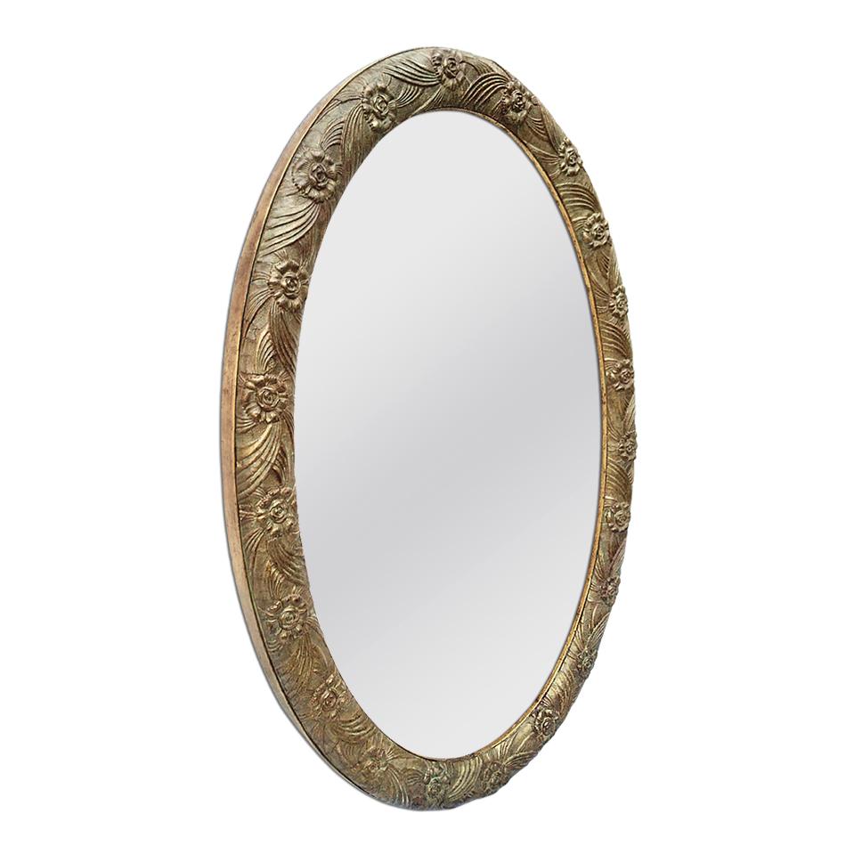 Art Deco oval French mirror with decor stylized foliages and flowers, circa 1930. Original gilding with patinated bronze leaf. Antique frame width 5 cm / 1.96 in. Modern glass mirror. Antique wood back.