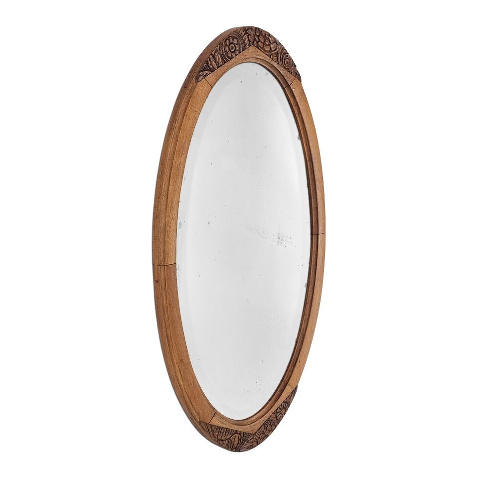 Elegante espejo ovalado francés de los años 40 de madera de peral. Su marco presenta decoraciones florales talladas, resaltadas por un acabado bicolor (un juego de tonos claros y oscuros en las tallas). Anchura del marco: 5,5 cm / 1,96 pulg. Espejo