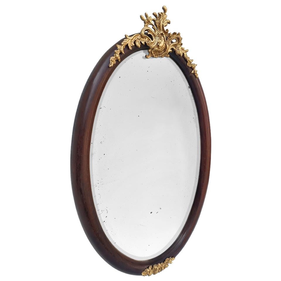 Antique French oval mirror, circa 1860. Mahogany wood oval frame with gilded bronze ornaments. Shell Louis XV style in gilded bronze at the top and frieze of flowers in the bottom. Antique frame width 4.5 cm / 1.77 in. Antique beveled glass mirror.
