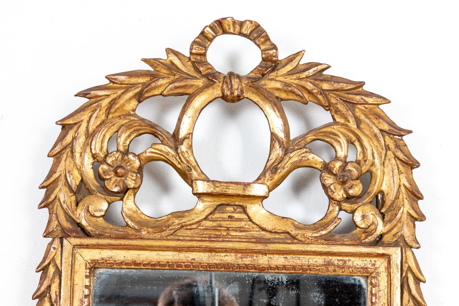 Circa 1900s antique French Louis XVI style parcel gilt mirror with classical detailing of laurel branches and flowers on top crown. Made in France. Please note of wear consistent with age including patina to the frame and mirror plate.