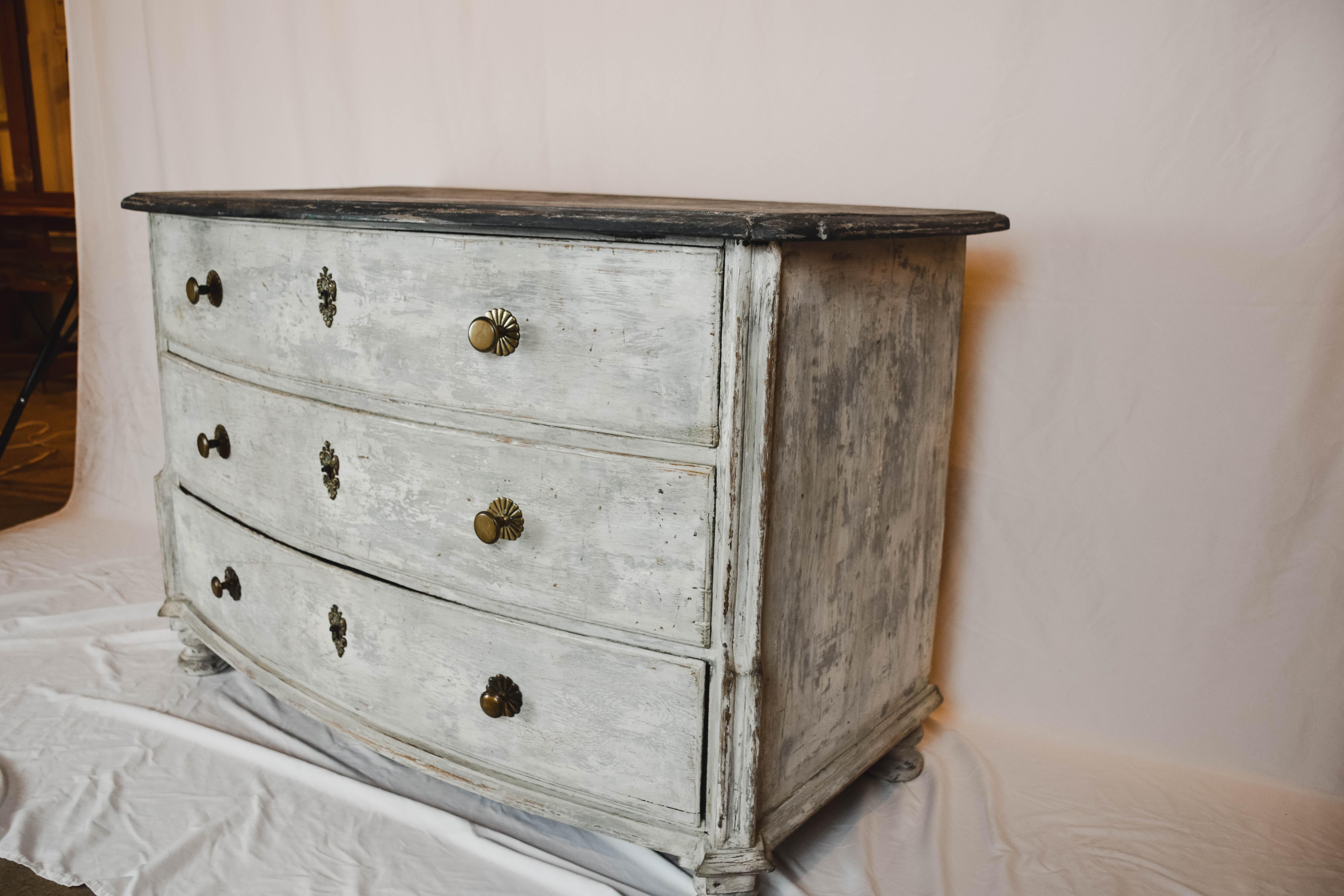 This is an antique French painted chest of drawers or commode. The chest of drawers has been painted in a French grey. Each of the three drawers feature two brass pulls, a brass lock plate and a locking mechanism, although no keys are available.