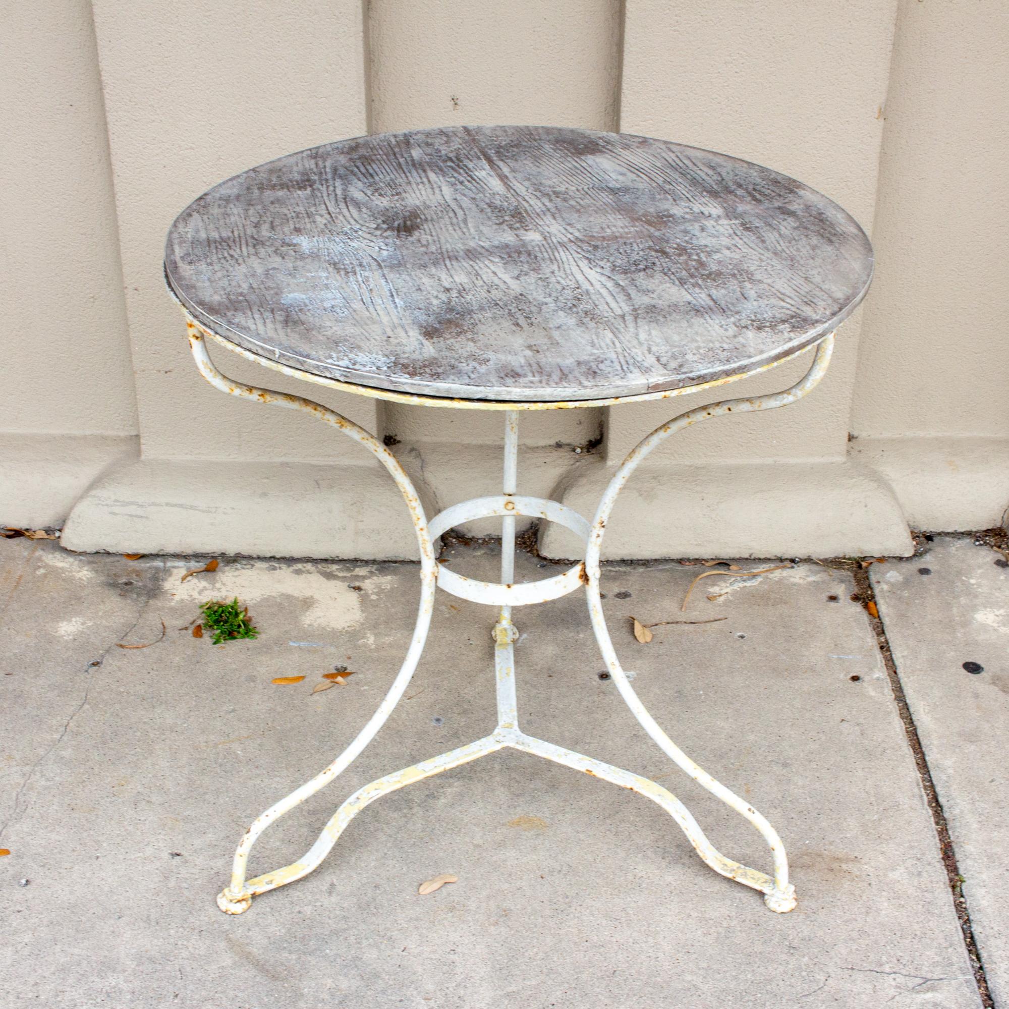 A Classic French iron bistro table, this piece features a painted iron base with three legs and a ring detail. The base has been painted both yellow and white and has some discoloration and patination (shown in the images) and some rust is present.