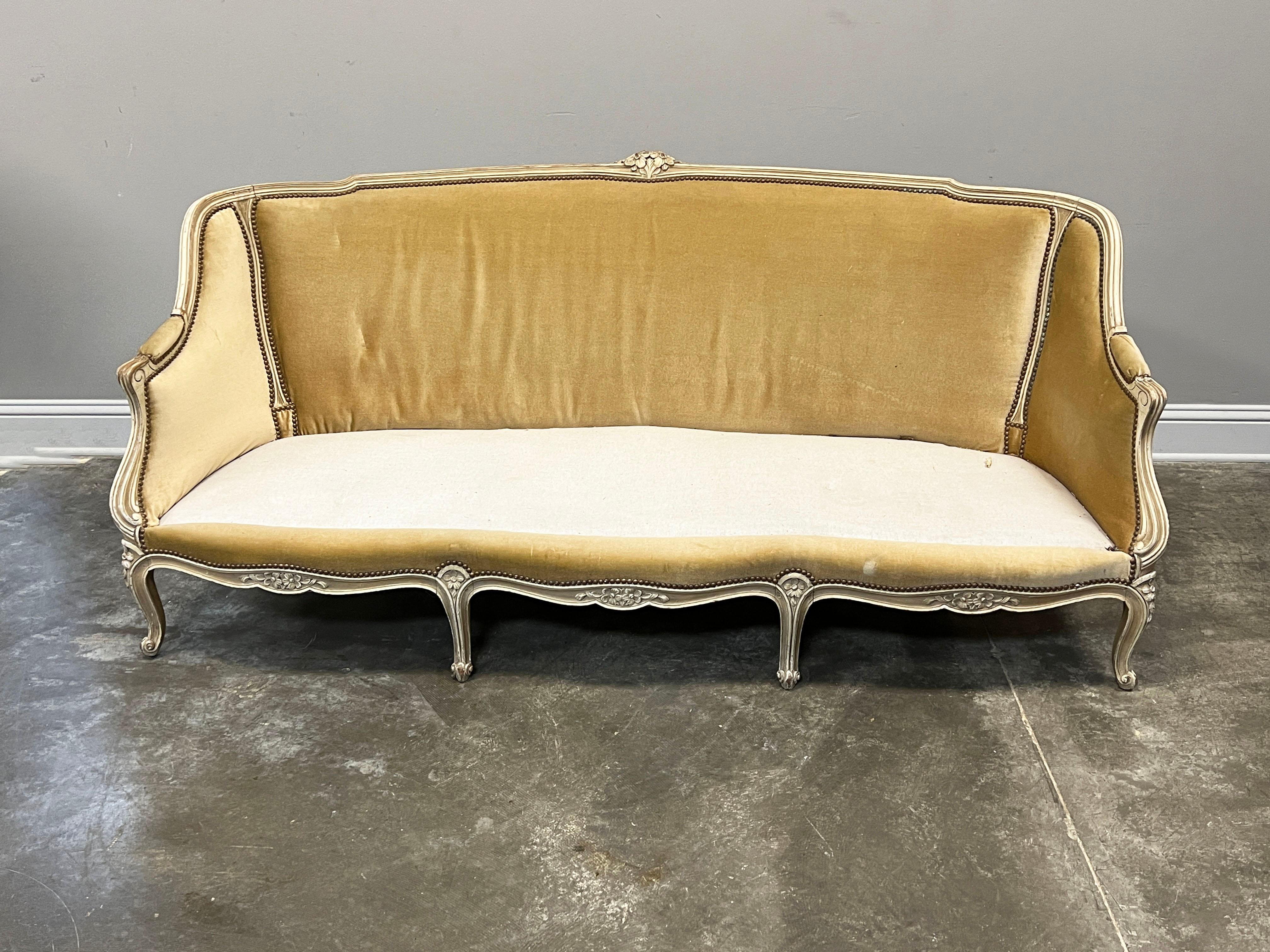 Antique 20th century French Louis XV style carved wood canape with original paint. Canape has lovely carved floral accents along the frame, top and bottom, along with eight cabriole legs consistent with the Louis XV style. Original velvet upholstery