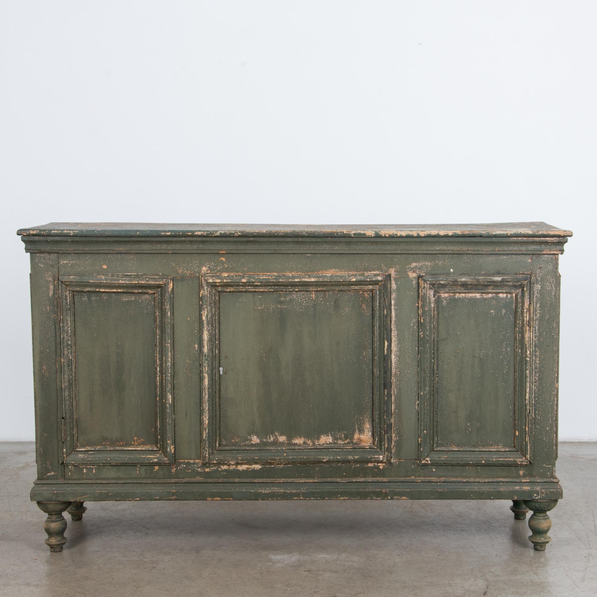An intriguing shop counter from France, circa 1900. A textured green paint, worn by time, dresses a frame and panel case resting on decorative turned feet. This is a unique piece with great character, converted from a three door buffet to a solid