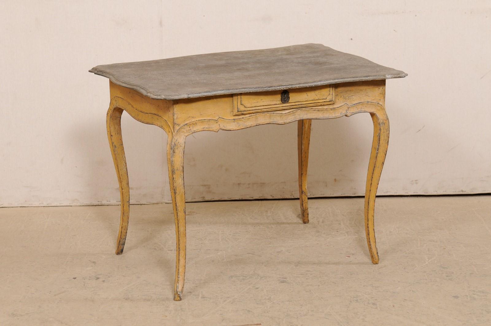 Une table française en bois peint de petite taille, avec un seul tiroir, du tournant du 18e et 19e siècle. Cette table ancienne de France présente un plateau de forme rectangulaire avec un joli bord festonné, qui surplombe le tablier festonné qui