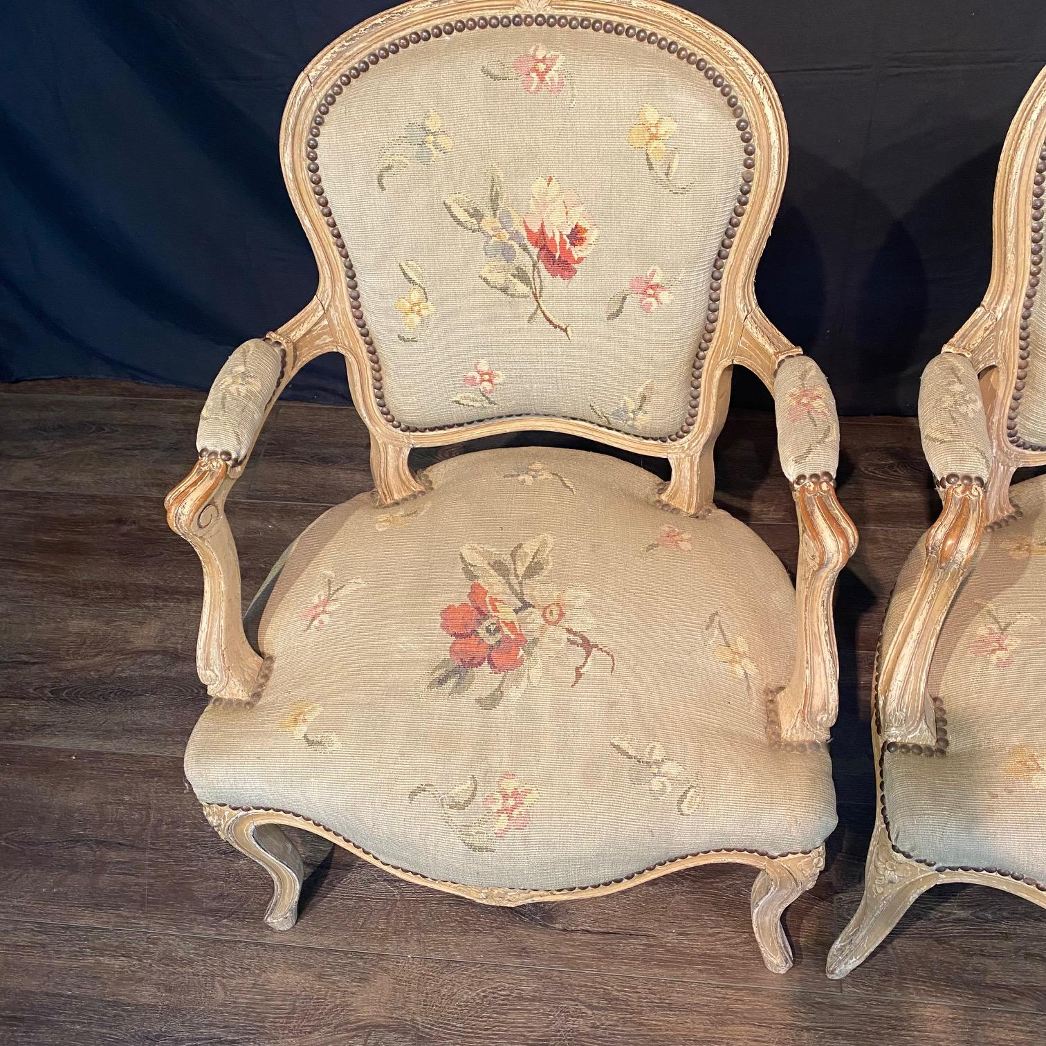 Elegant pair of French Louis XV armchairs or fauteuils with exquisite (yet sturdy) Aubusson floral tapestry upholstery.  This stunning pair of carved walnut painted armchairs captures the essence of classic French design, enhanced by a soft,