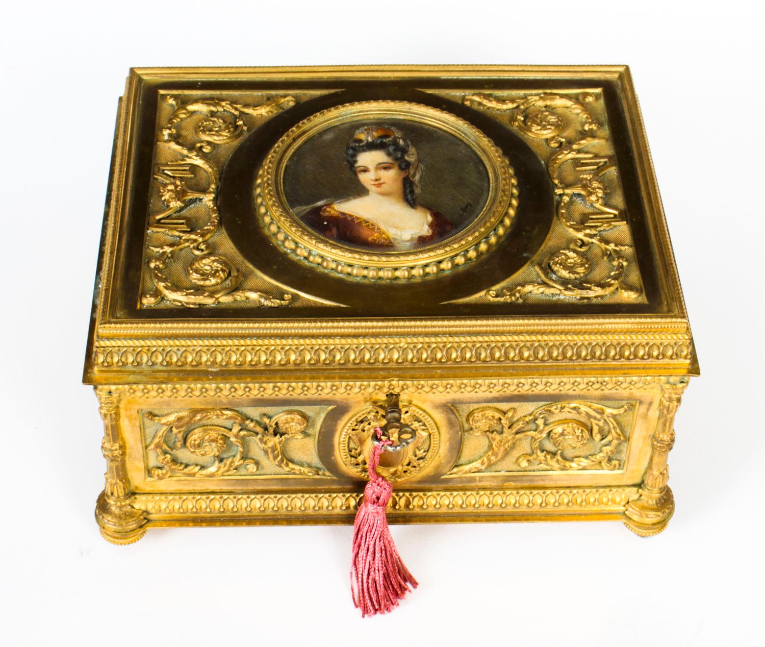This is a beautiful antique French Palais Royale gilded bronze ormolu jewellery casket, circa 1820 in date.

The sides are decorated with armorial panels, scrolled acanthus leaves and floral vases. The hinged lid is set with a large circular
