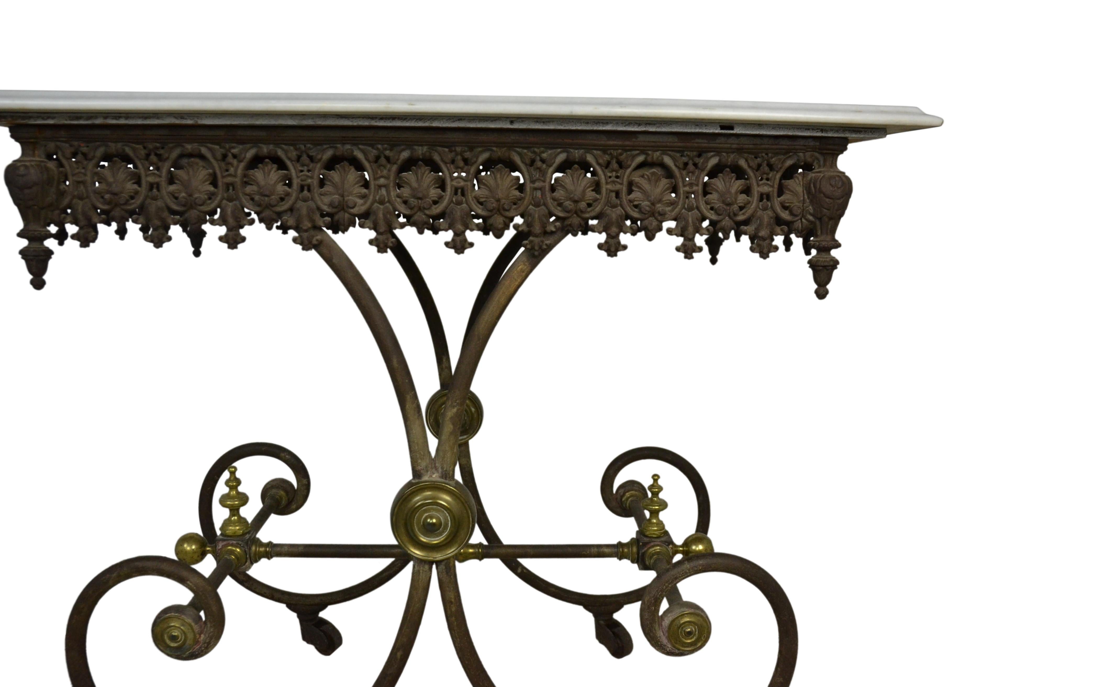 A quality antique French pastry table from the 19th century. Iron base with brass finials and medallions. Iron wheels or casters. Fretwork frieze decorated with leaf design. White marble top, 19th century.