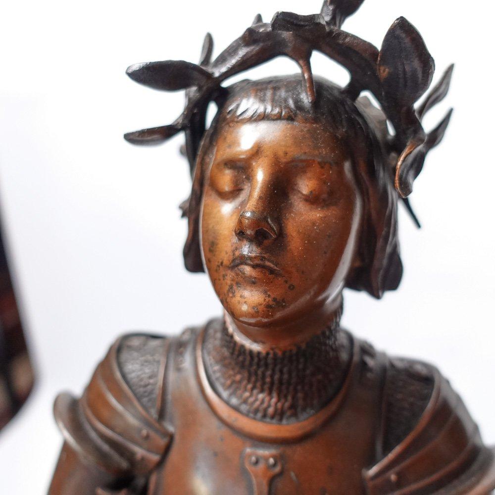 This large antique sculpture depicts the heroine Joan of Arc with perfect poise and dressed in full armor, complete with helmet, mail coif and sword by her feet. The plate armor is shown in all its intricate detail down to the extremely long, pointy