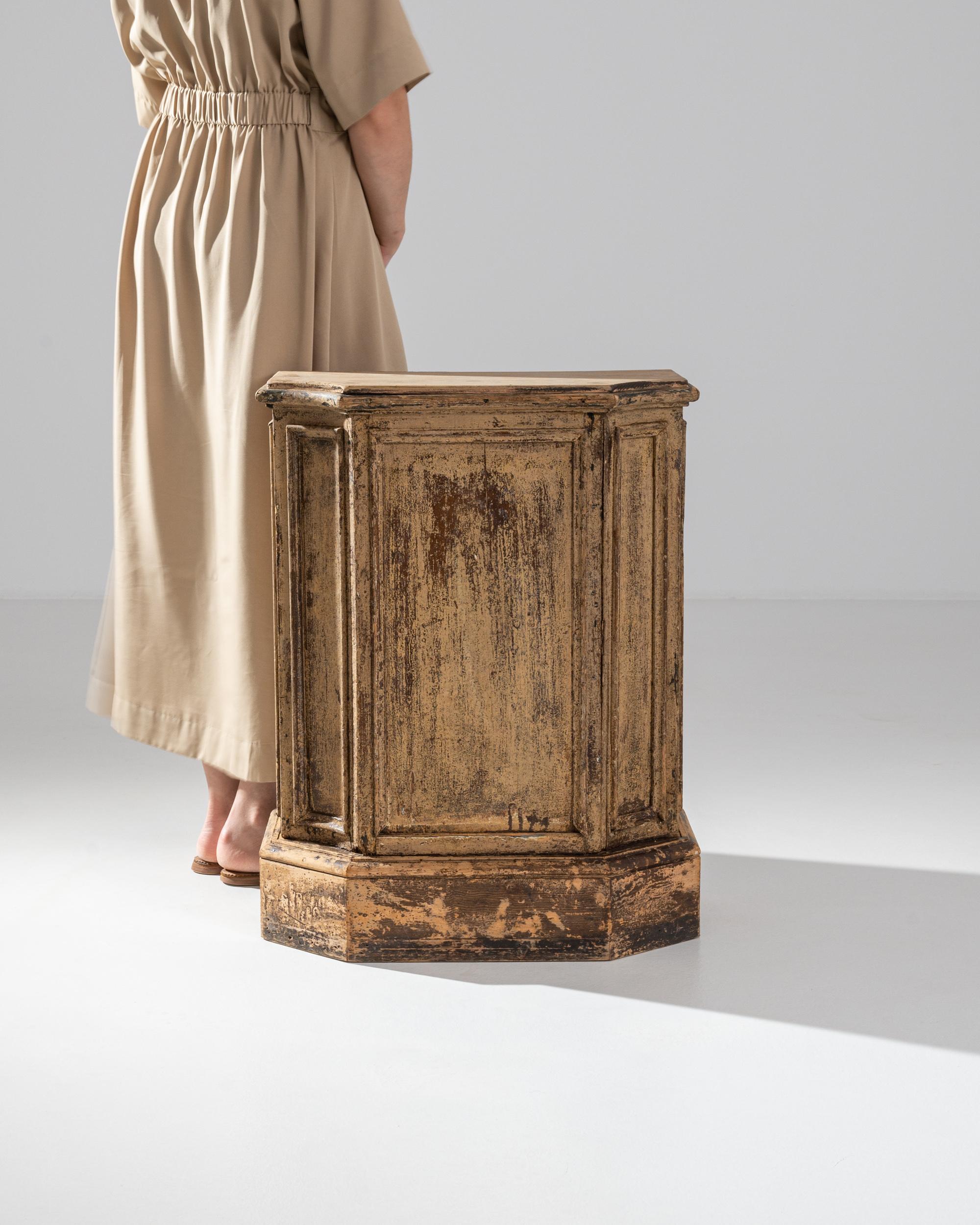 A wooden pedestal from 1800s France. Layers of caramel and warm brown across the pedestal’s surface have been revealed by time. Its trapezoidal shape gives the 27 inch tall plinth a projecting stance, ideal for display.