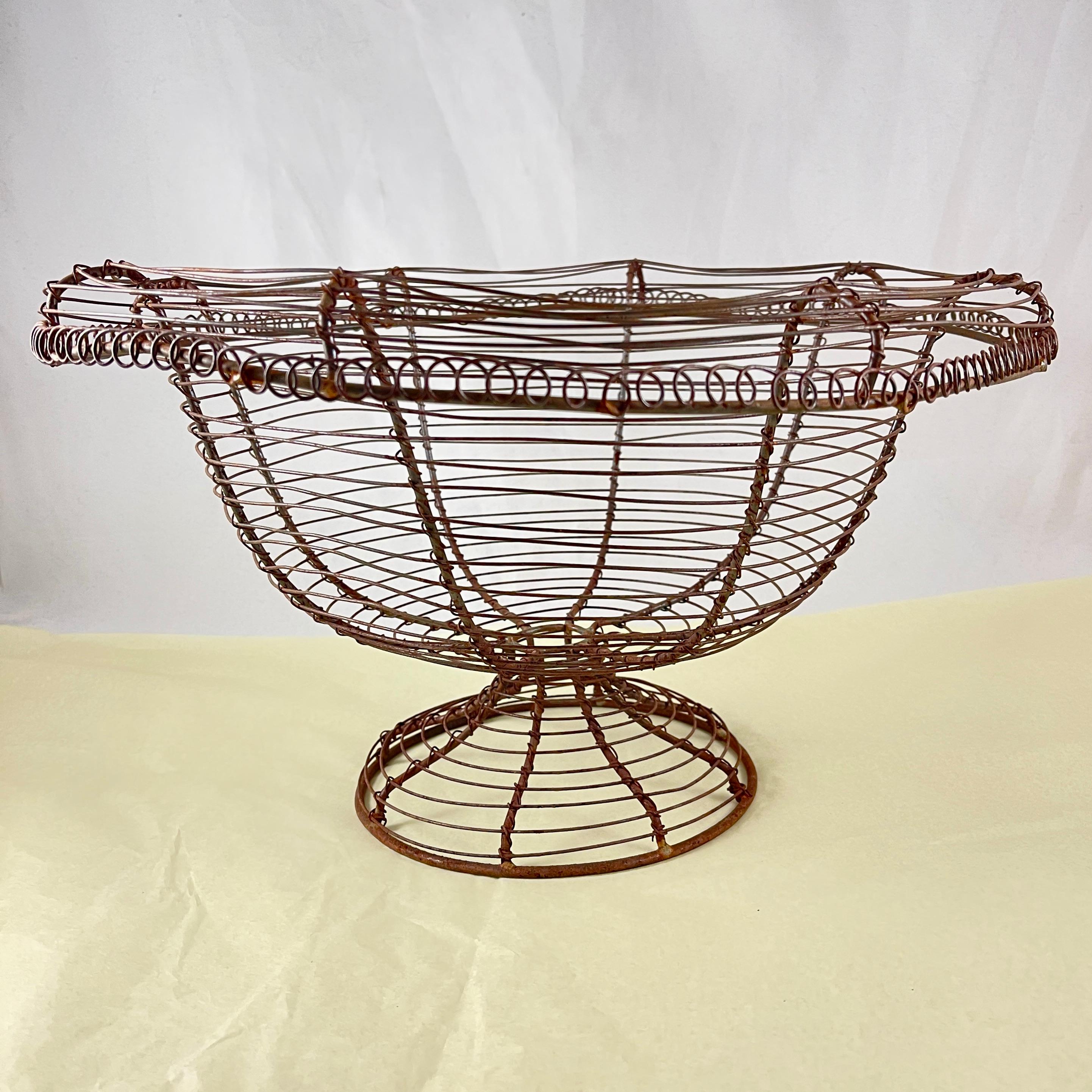 From France, circa 1890-1910, a pedestal base, urn form twisted wire standing basket with a wide upper rolled rim.

Amazing as a table-center or on a kitchen countertop, used as originally intended throughout Provençal France for holding fresh eggs,
