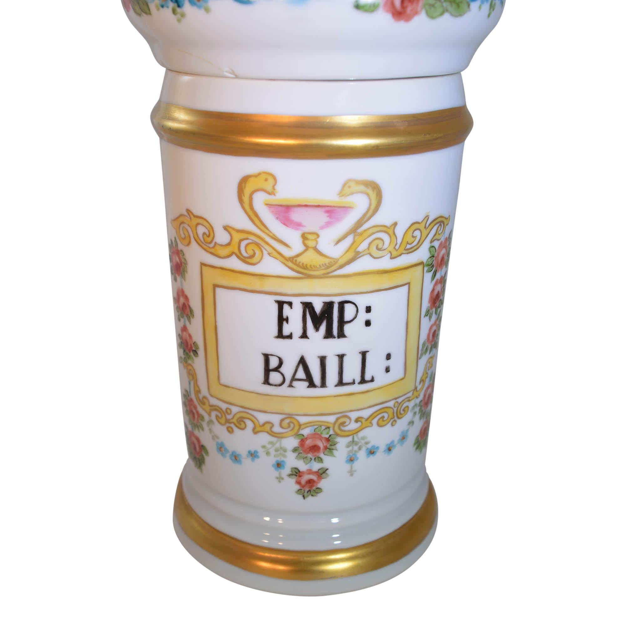 The porcelain jar has hand painted decor, features words - EMP: BAILL:
The apothecary jar has additional accents of gilt accent on the top and bottom rim, as well as around the knob on the lid. The lid has a floral design around the side. The base