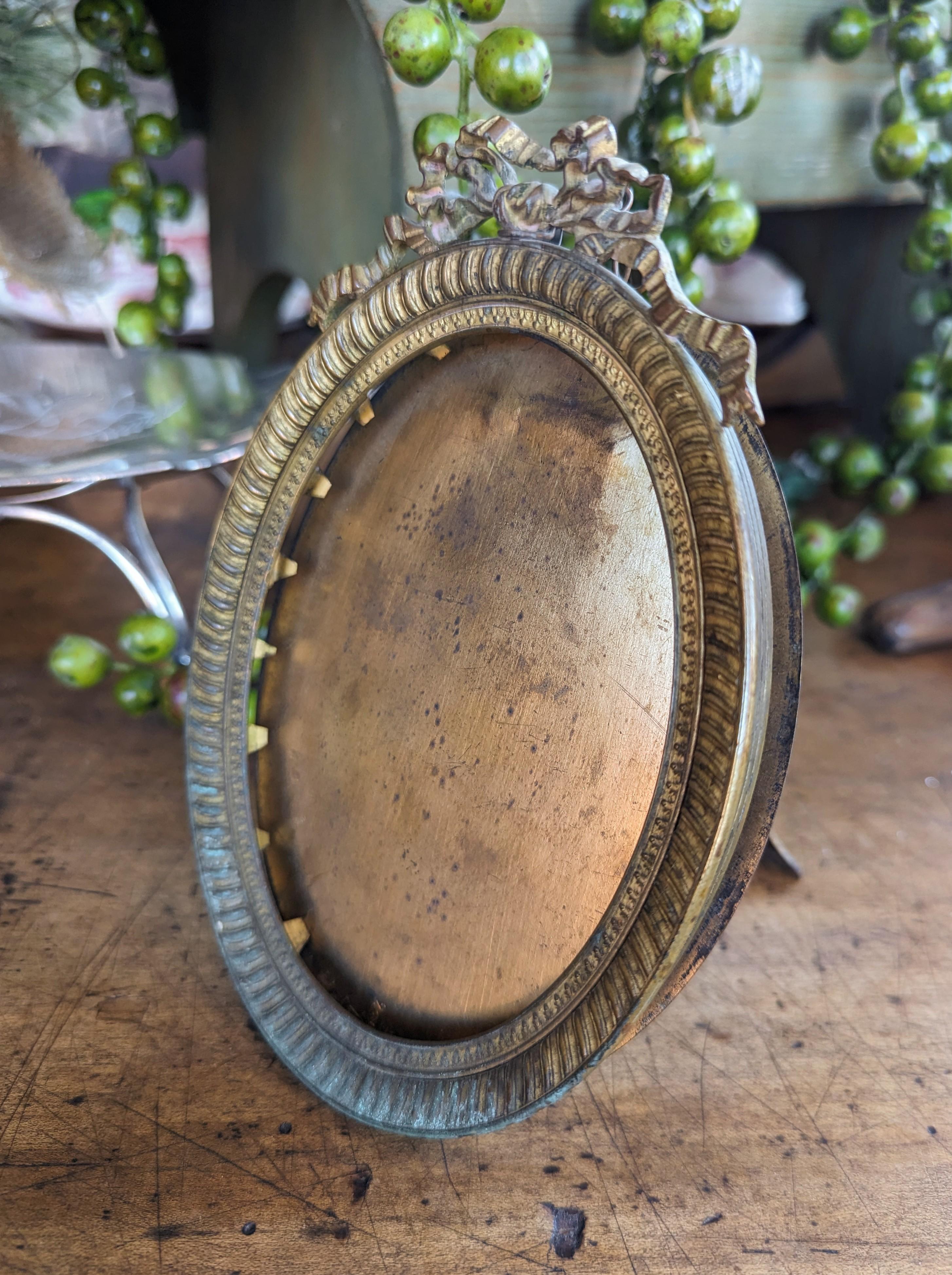 Beautifully detailed antique French bronze easel back picture frame, circa late 1800's. This oval photo frame features a ribbon and bow design in the Louis XVI style. Measures 6.5 inches from top to bottom, by 4.6 inches in total width, by