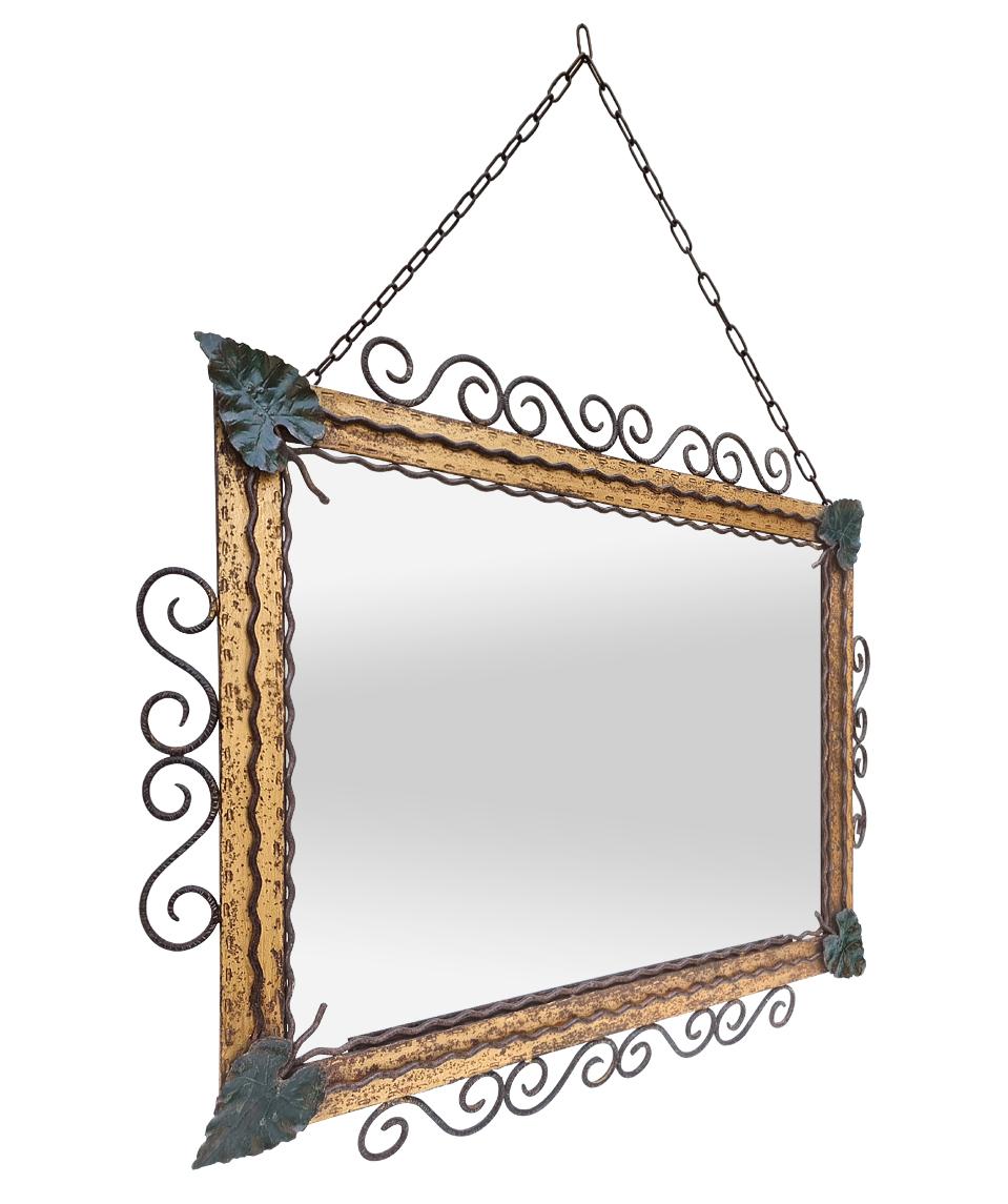 Rare antique wrought iron mirror, French origin circa 1940. Antique forged metal frame of gilded and green colors orned with stylized volutes and vine leaves in the corners. Original antique chain. Modern glass mirror (perfect reflection). Wood back.