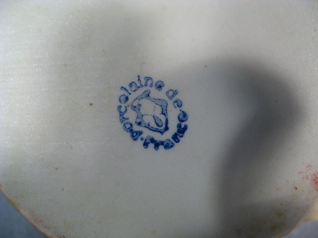 Este encantador juego de condimentos de porcelana francesa antigua, de la primera mitad del siglo XX, presenta una encantadora representación de una campesina que se dirige al mercado. Un recuerdo de La Louvesc, esta pieza única añade un toque de