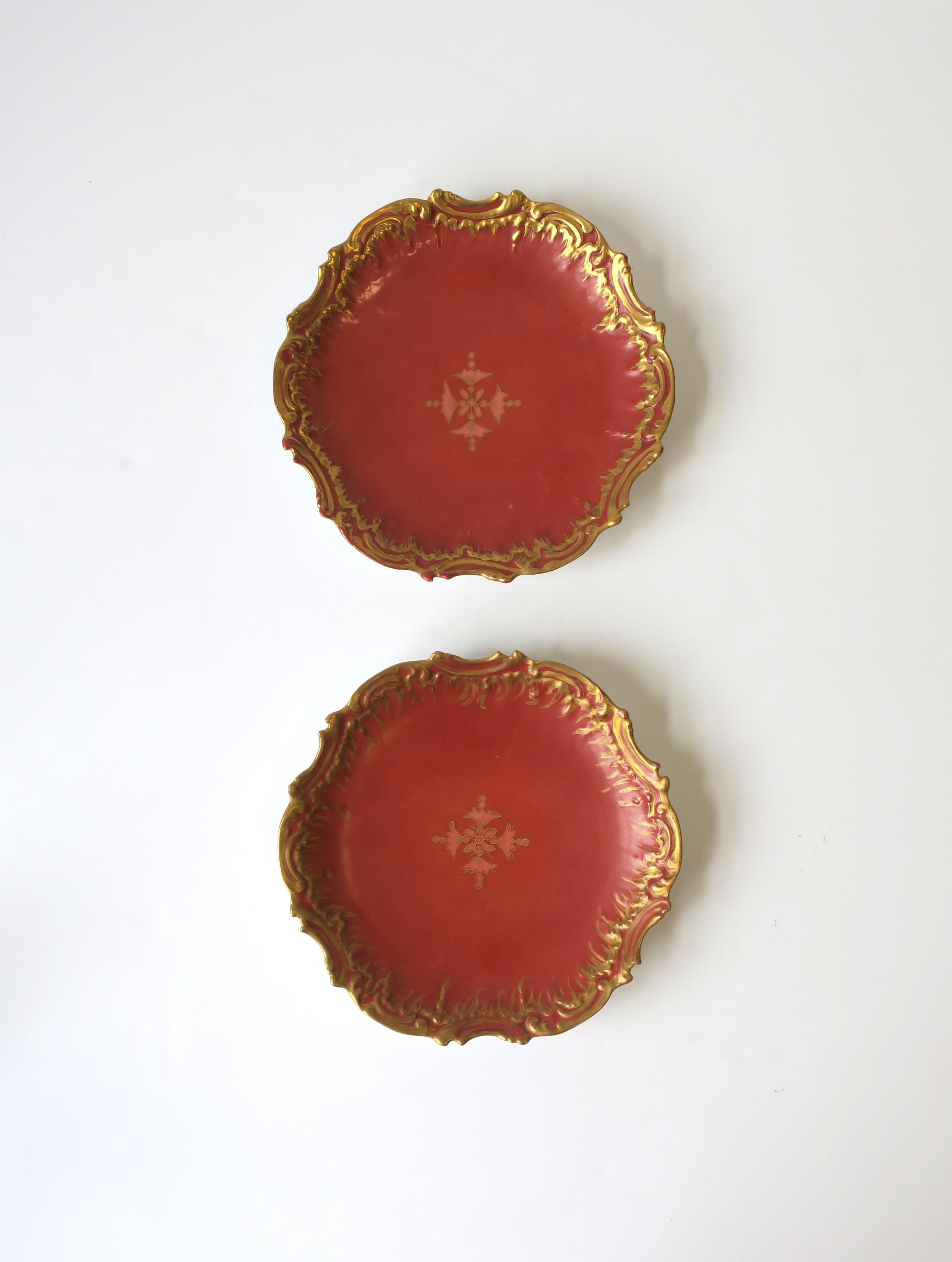 A beautiful pair of antique French Limoges porcelain plates, circa 19th century, France. Plates are predominantly a terracotta hue with a carnation pink center design, and a hand-painted gold raised decorative edge. A great set for entertaining, as