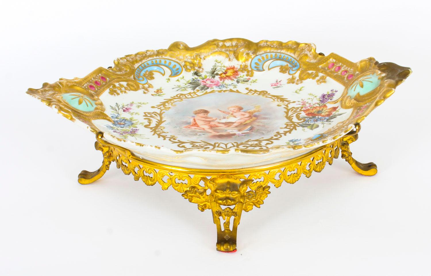 This is an impressive and highly decorative French porcelain and ormolu mounted centrepiece, mid-19th century in date.
 
It is in Limoges style and features a beautiful classical scene in the centre with cherubs surrounded by flowers in a rococo