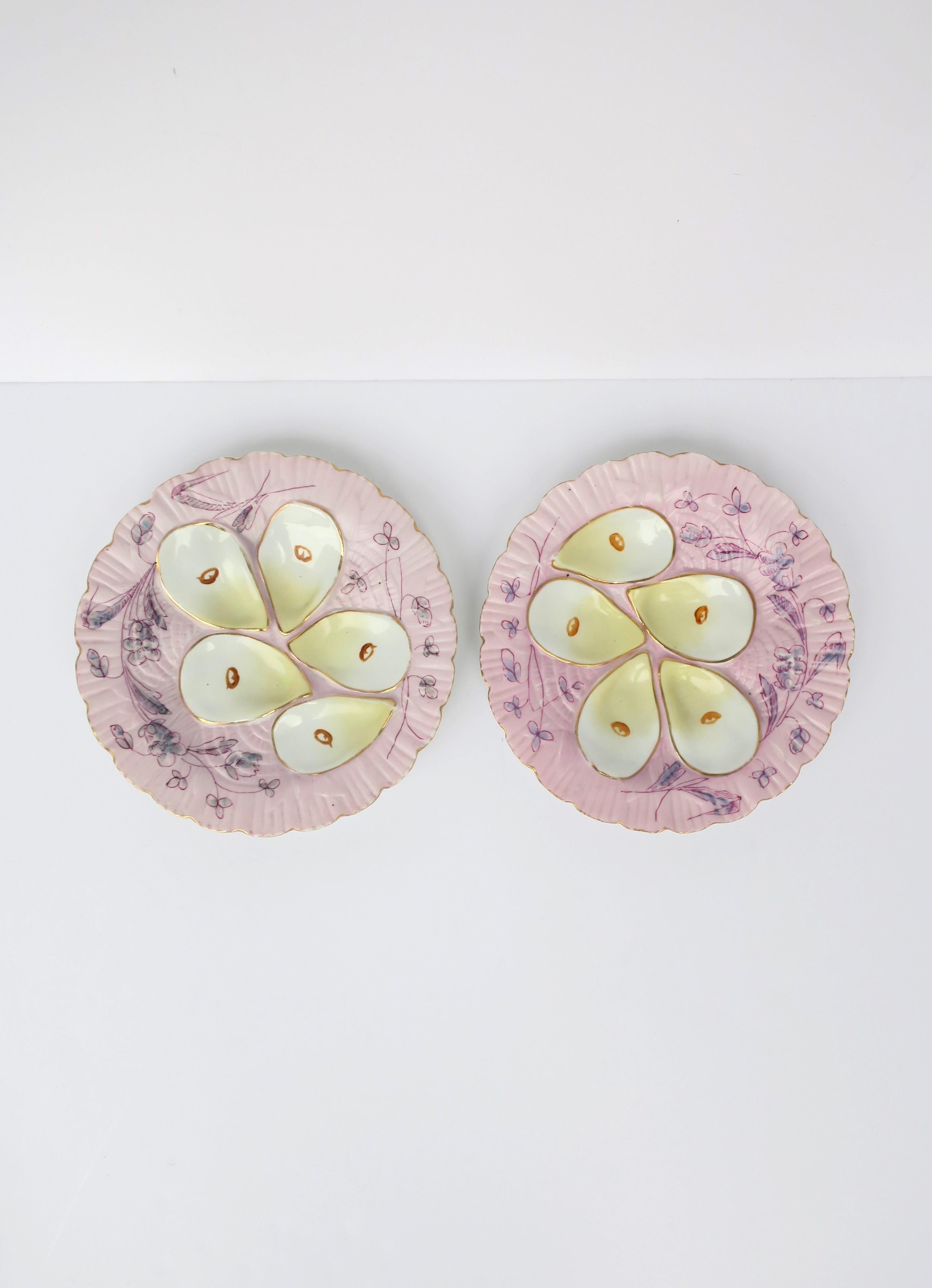 A beautiful set of two (2) antique French porcelain oyster plates, circa early-20th century, France. Plates are white porcelain decorated in pink and light purple hues, organic flower and leaf design around, and 5 wells edged in gold with a