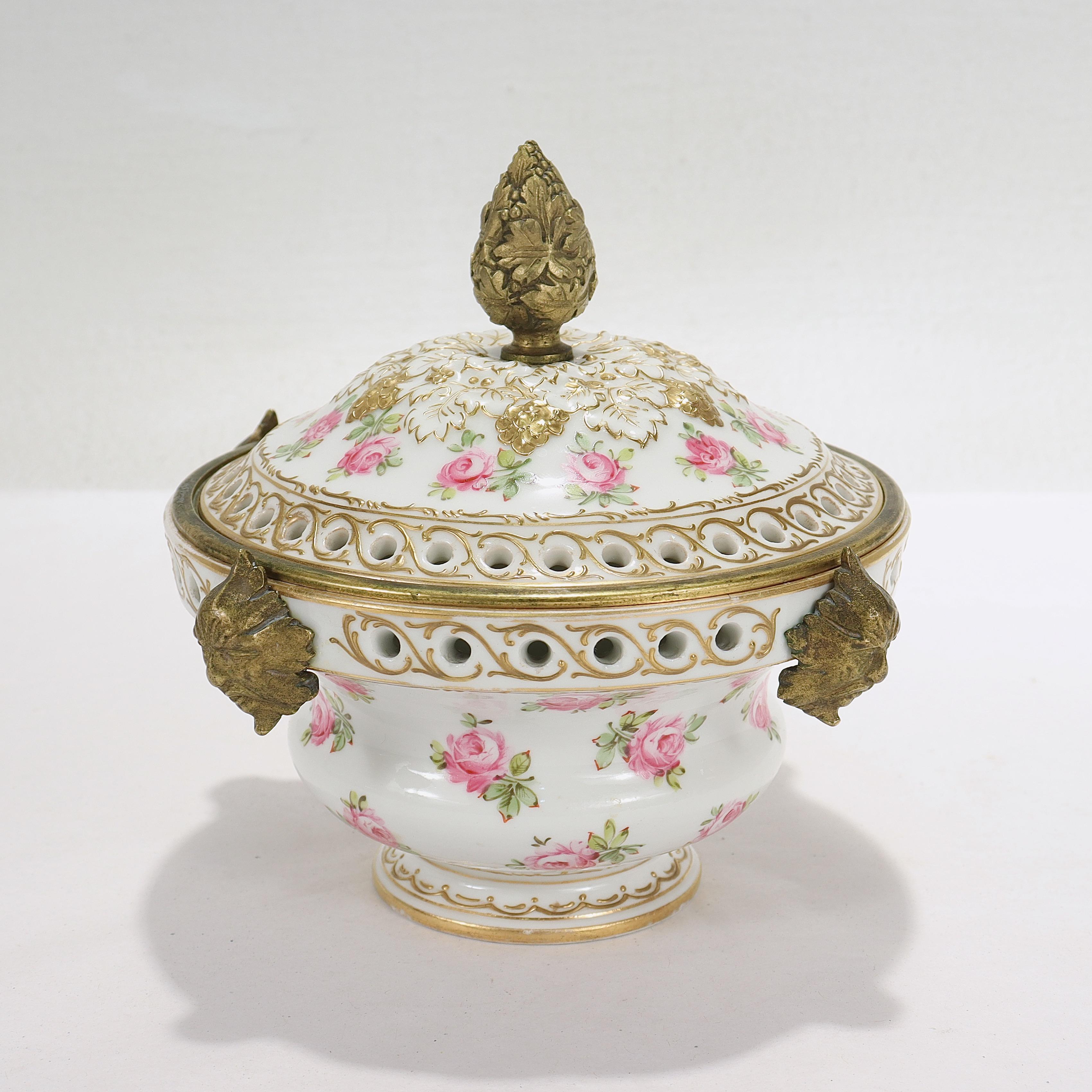 A fine antique French porcelain potpourri cachepot.

In the Sevres style.

Mounted with a bronze finial to the lid, 4 bronze masks to the circumference, and set with a removable bronze ring to the interior lip.
