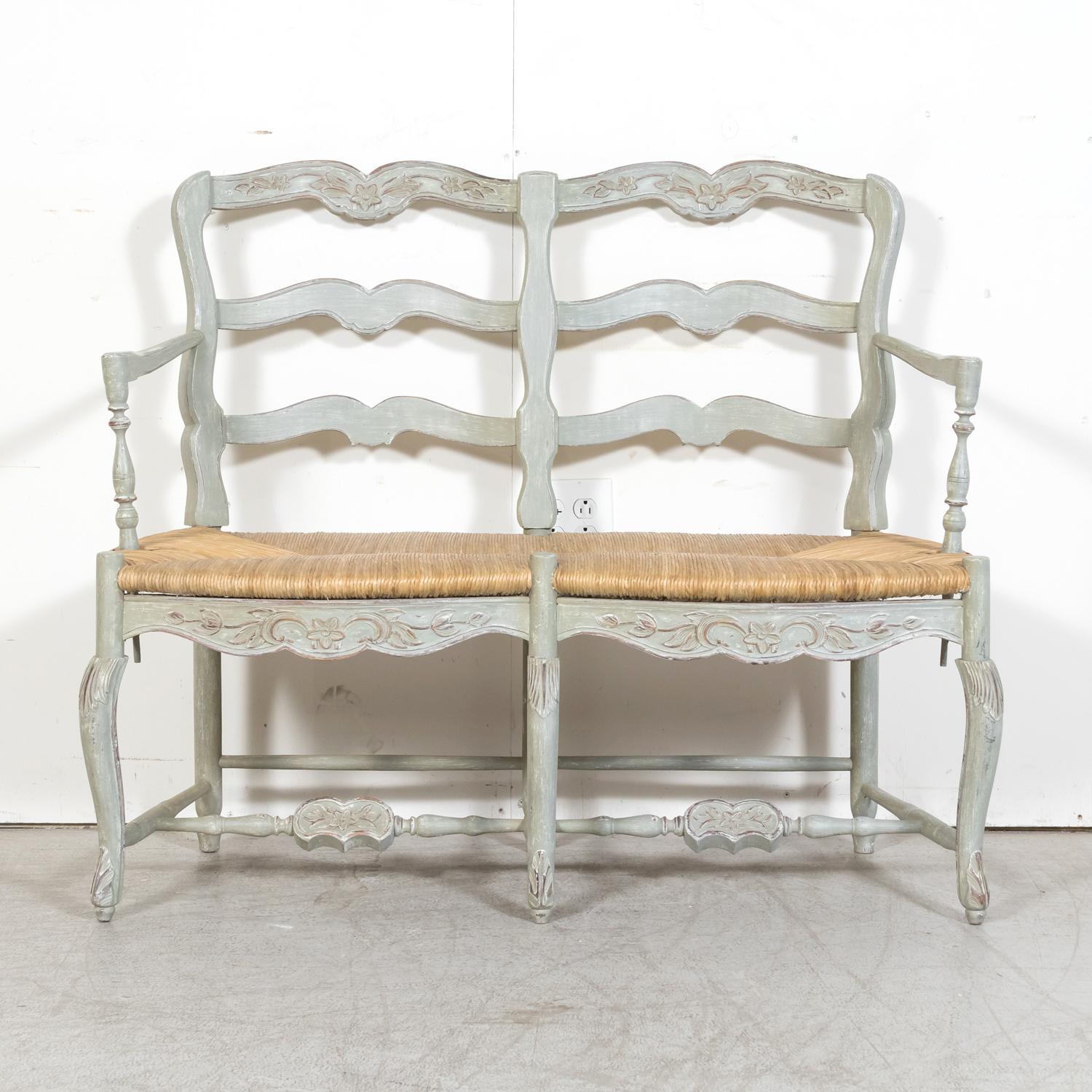 An antique French Louis XV style carved settee or radassier from Provence, circa 1920s. Having a classic French Country ladder back design, this Provençal bench is painted a beautiful bluish green color and features traditional floral and foliate