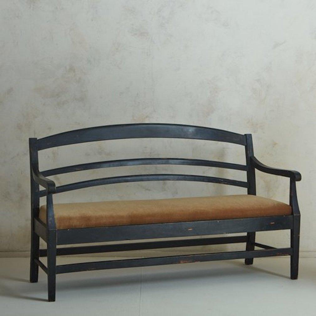An antique French provincial bench featuring a black painted wood frame with an arched ladder back, curved arms and stretcher details. The seat was newly reupholstered in a handsome cognac mohair. Sourced in France, early 20th Century.

