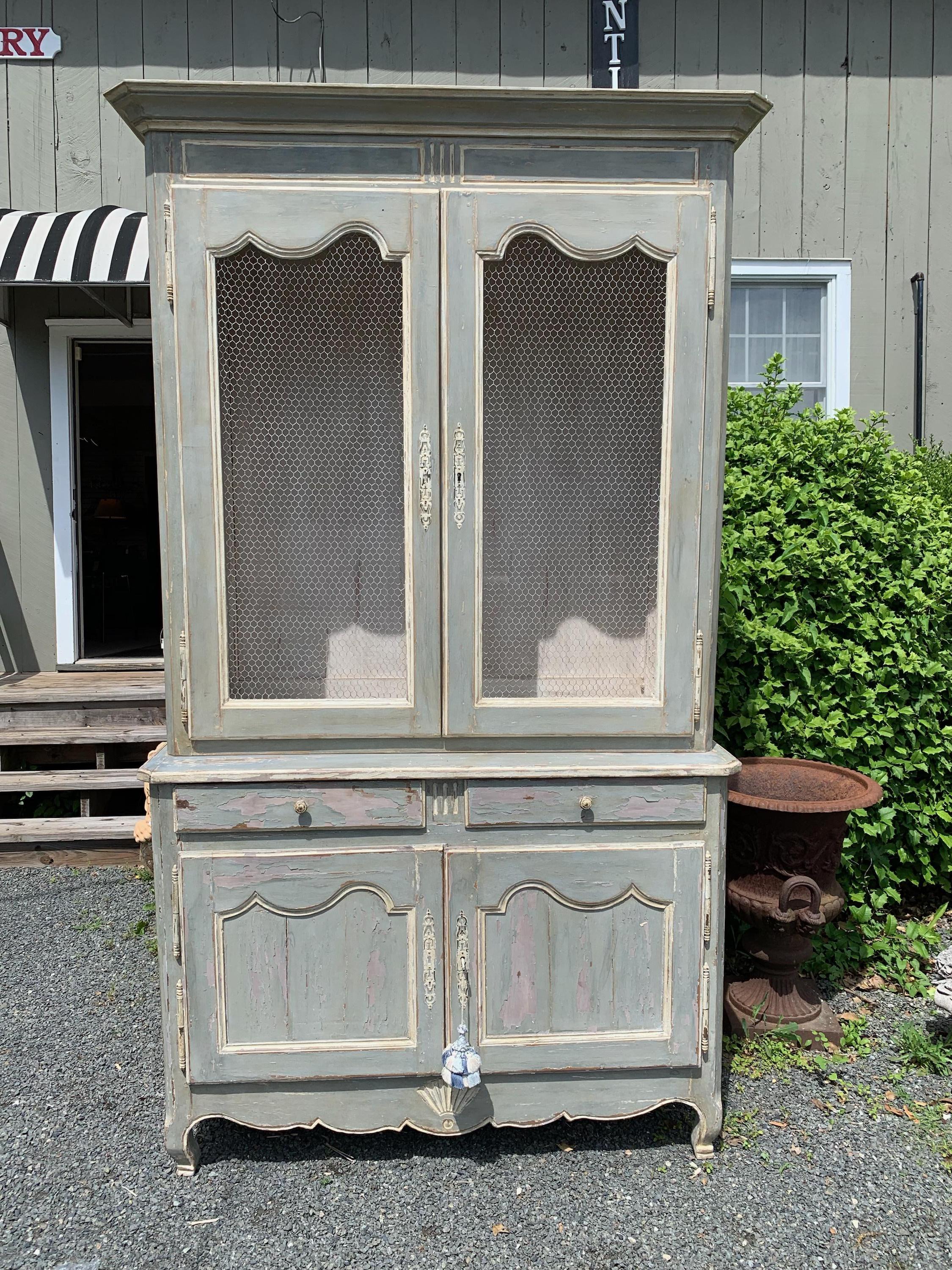 Charming 19th century French Provincial kitchen cupboard, hand carved and hand painted a Provençal grey blue with white painted interior and details, having chicken wire in the doors and shell motif on the apron. There are shaped panel tops, a