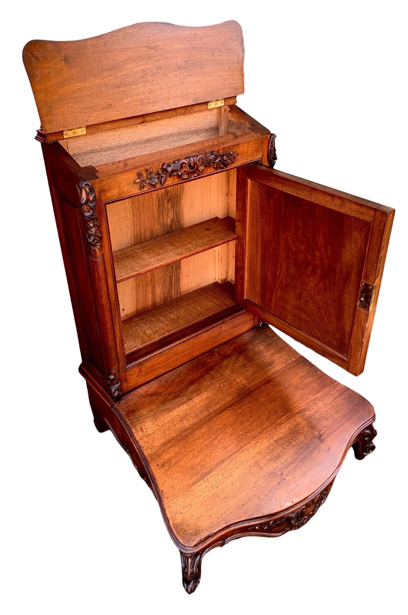 An stunning 19th century hand carved walnut Prie Dieu (Literally French for pray God) having a pierced cruciform crest over a slant top lifting arm rest opening to storage, over a relief and scroll carved cupboard door, above a wide kneeler, on