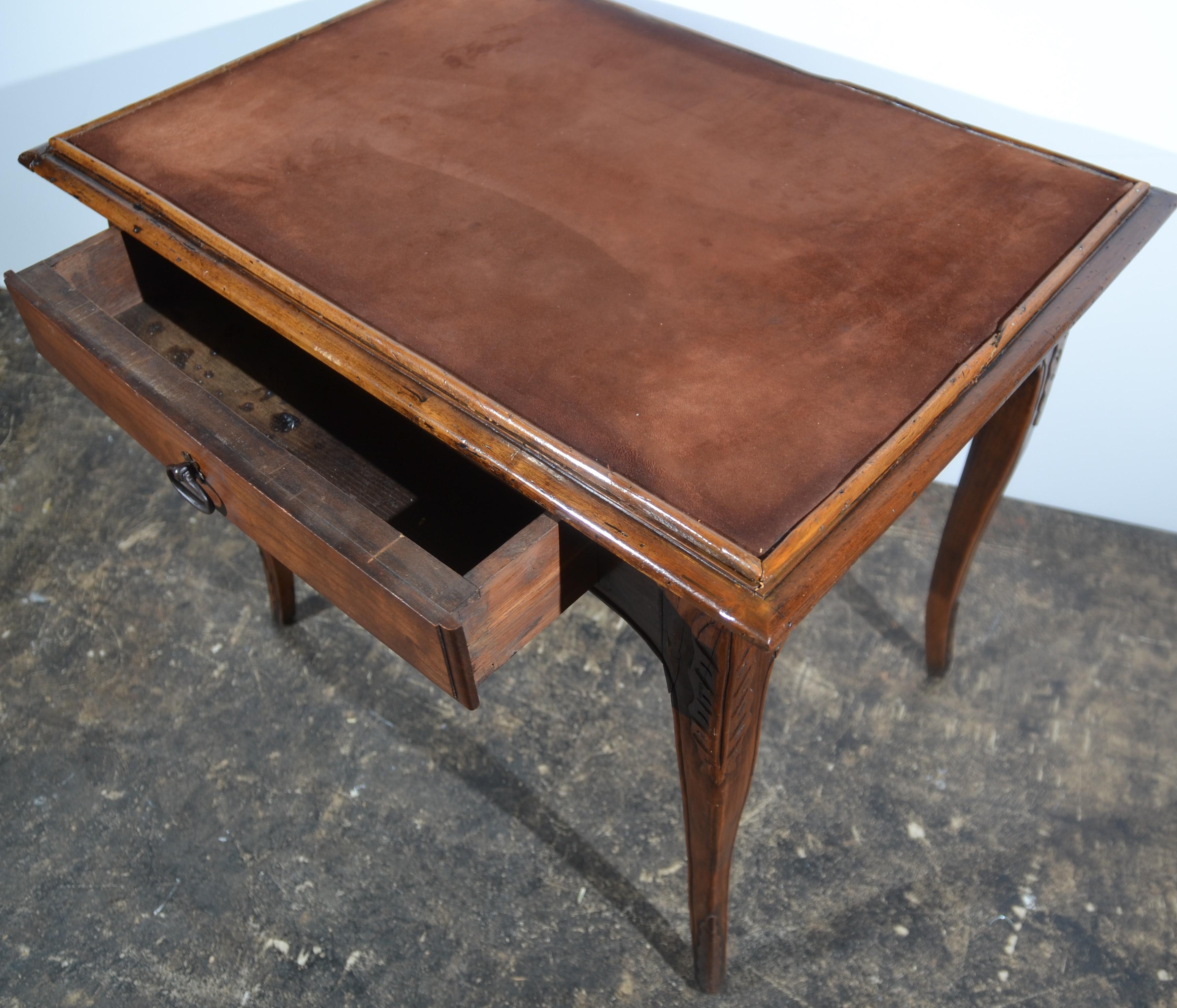 A late 19th century French Provincial side table or ladies desk in fruitwood. Single drawer with original iron loop handle. Acanthus leaf carving to the legs and below the drawer. Shell style carving to the sides. The top with an applied brown soft