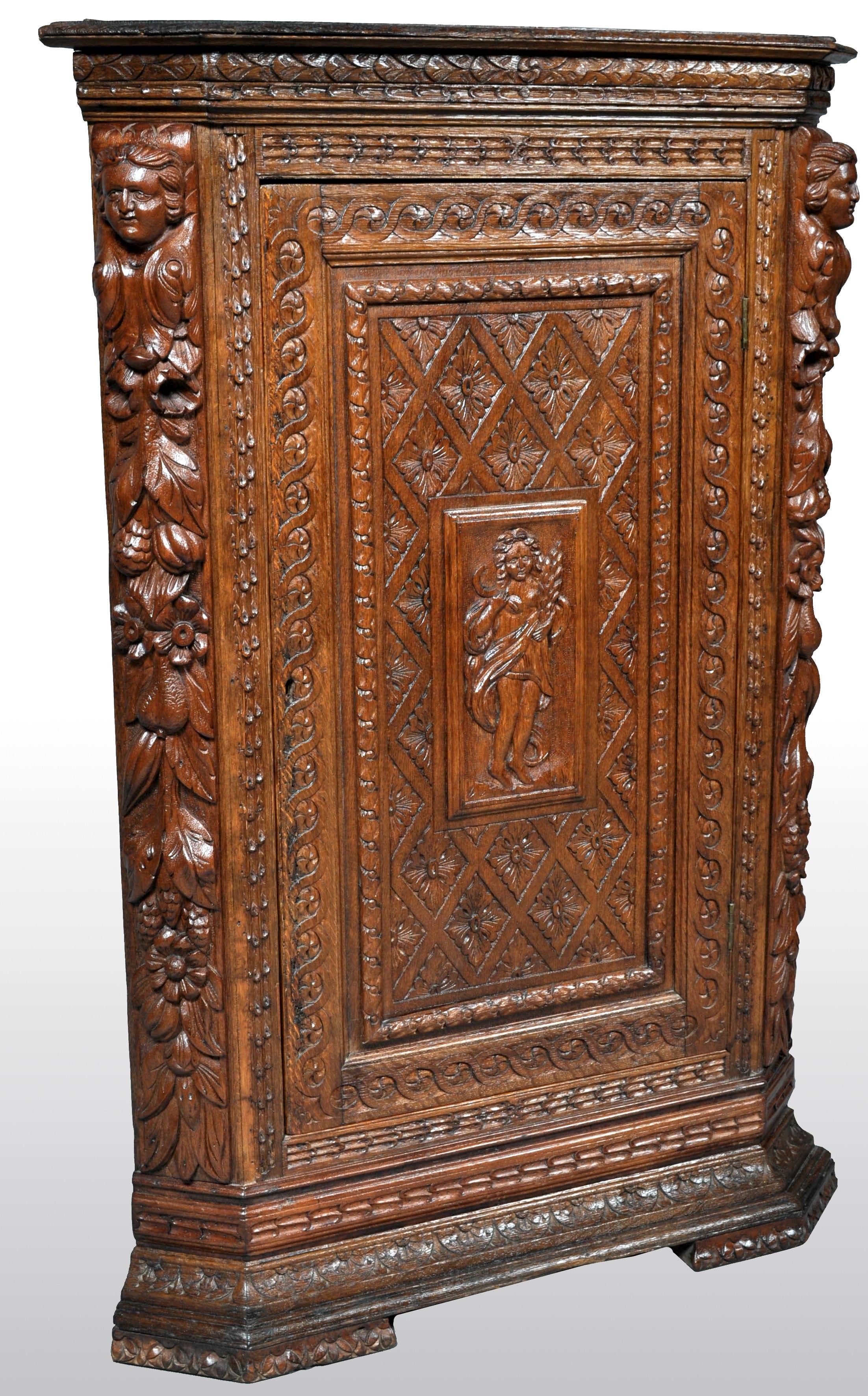 Antique French baroque carved oak corner cabinet, circa 1780. The top of the cabinet having a low gallery and below highly carved figural and fruiting garland pilasters to either side. The cabinet having a single door with bands of intertwined