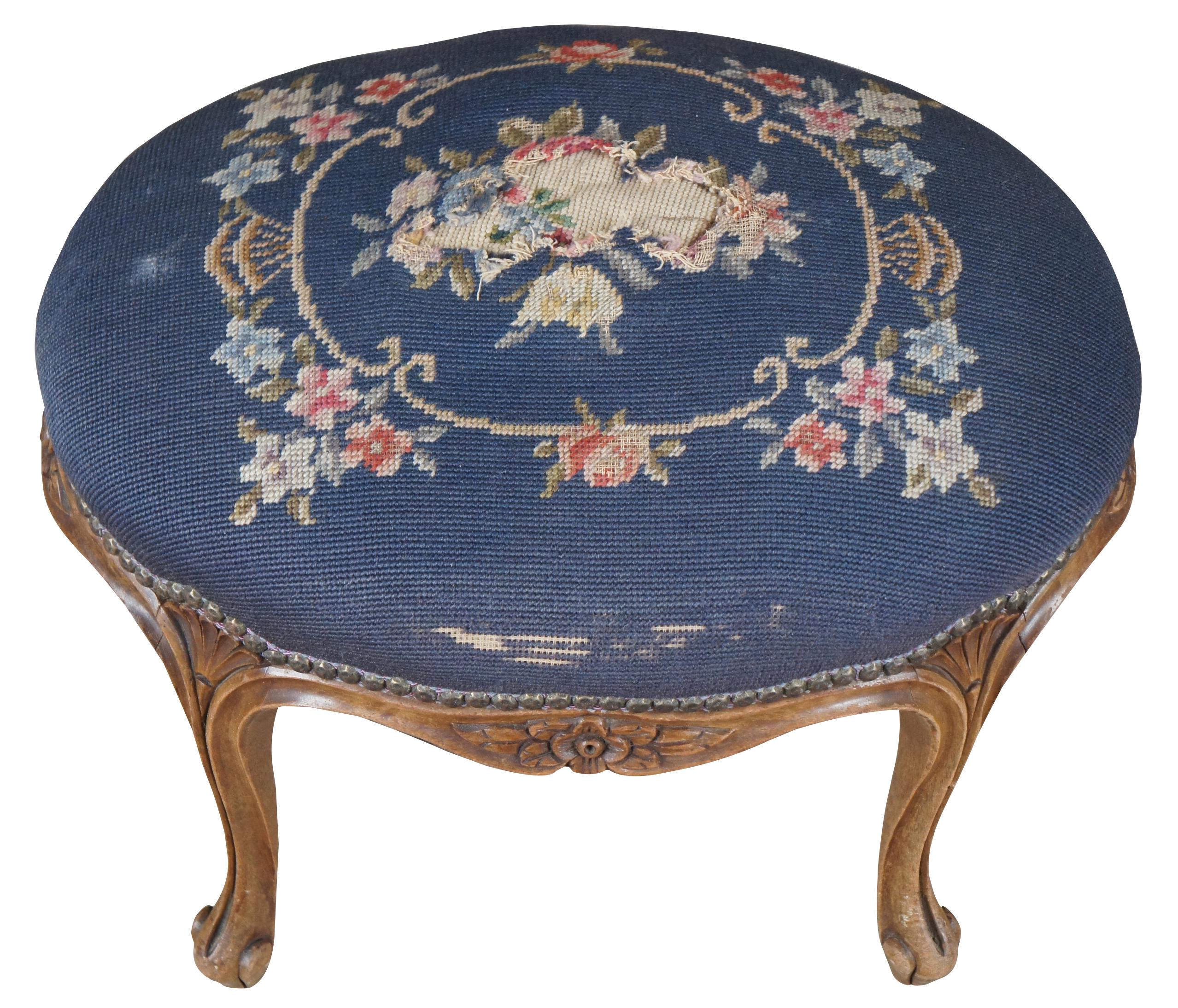 Antique French Provincial stool, foot rest or ottoman. Made of walnut featuring French styling with serpentine form with carved floral, fluted and scalloped accents, and needlepoint floral embroidered upholstery framed in nailhead trim. Measure: