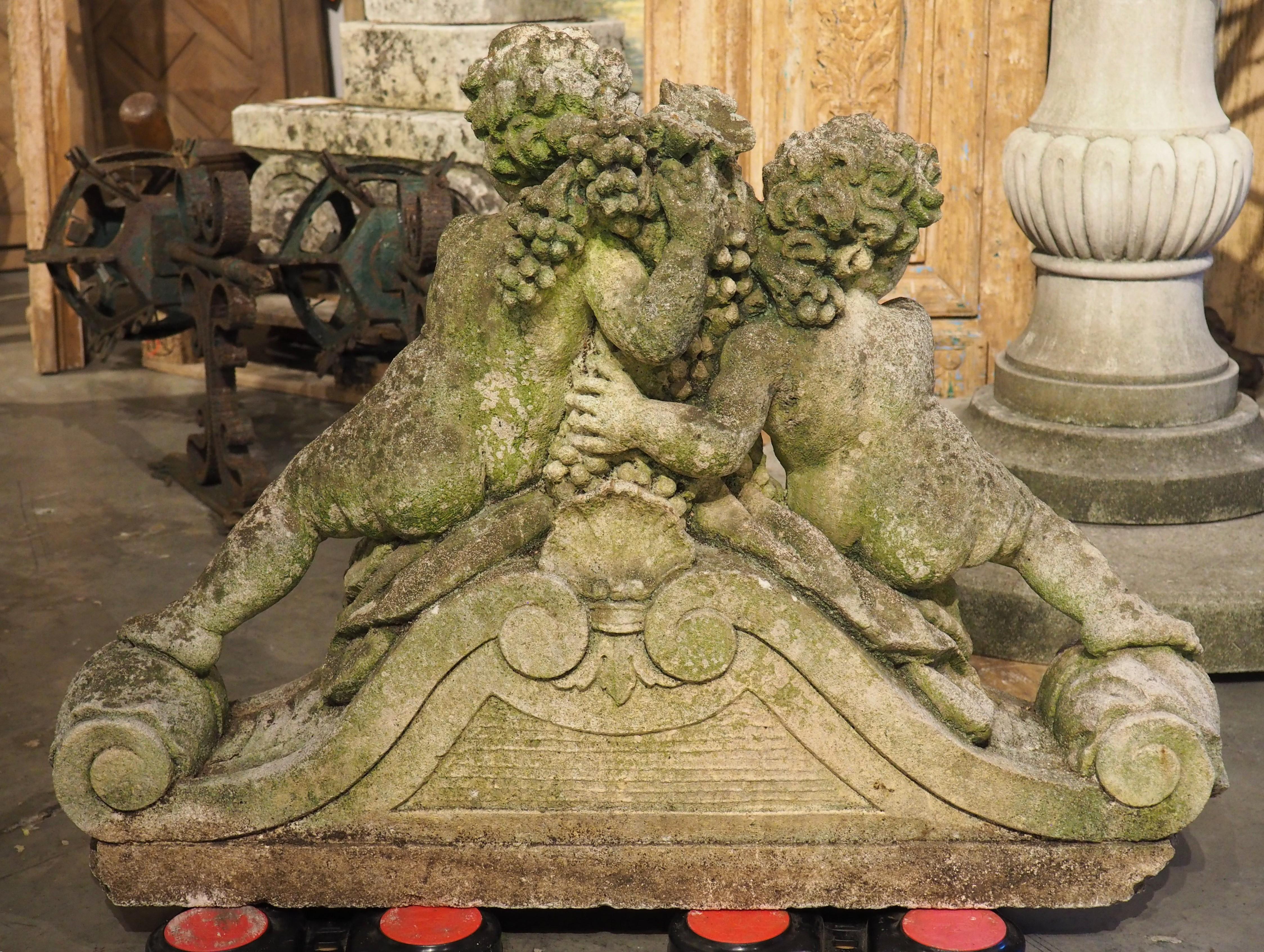 Made from reconstituted stone circa 1900 in France, this fountain element or garden statuary depicts two putti sitting on a long scrolled console. The innocent-looking cherubs are clutching a large cluster of grapes as they look off in the distance