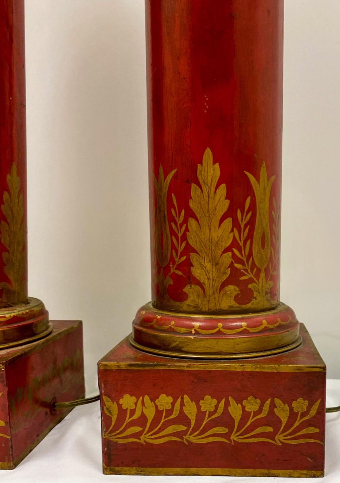 This is an antique pair of French neo-classical style red tole lamps with gilt stenciling. They have a classic cylinder form and are in working order.