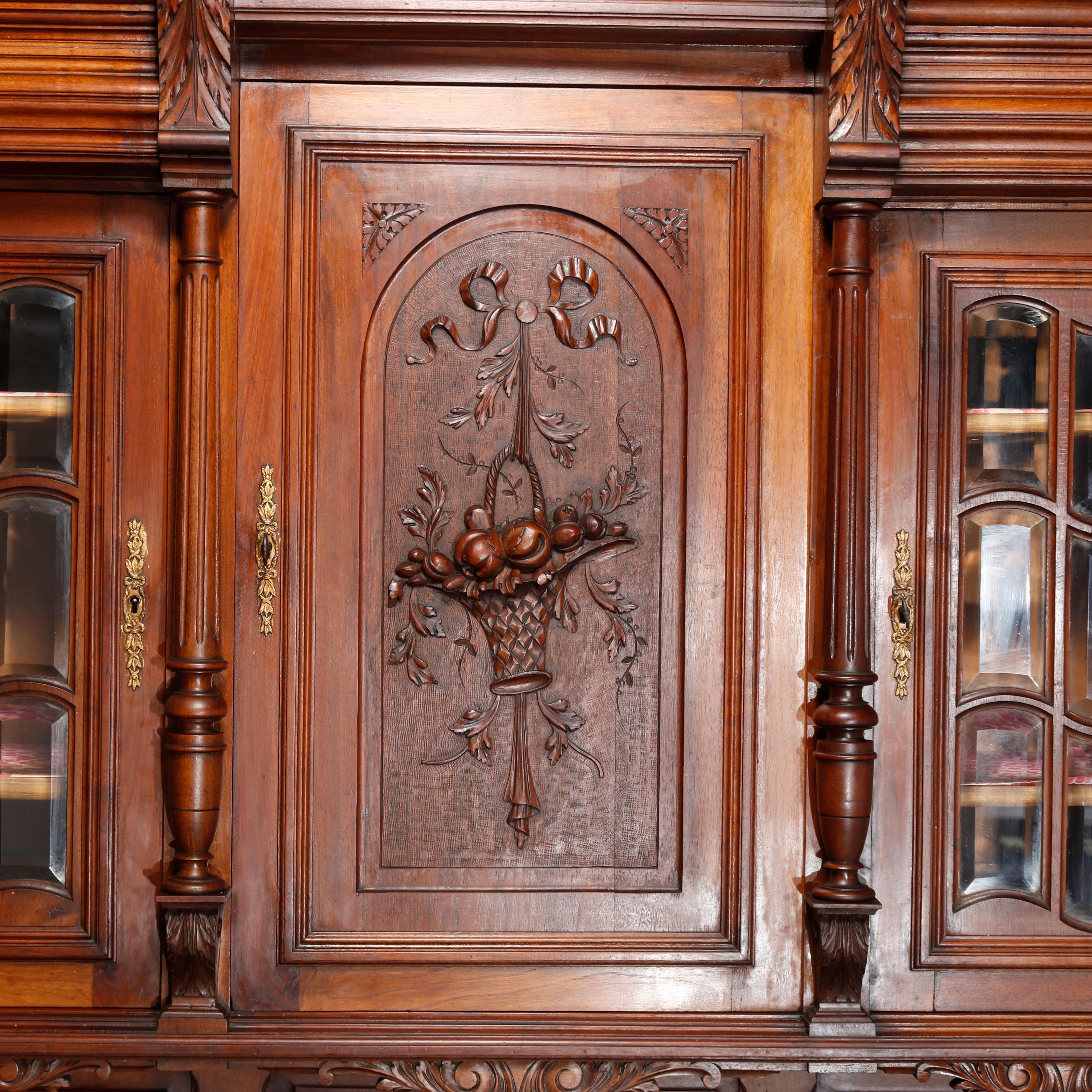Antique French Renaissance carved walnut court cupboard with scroll and foliate decorated crest flanked by acanthus, surmounting upper case having central door with panier de fleur flanked by fluted turned columns and mullioned glass doors with