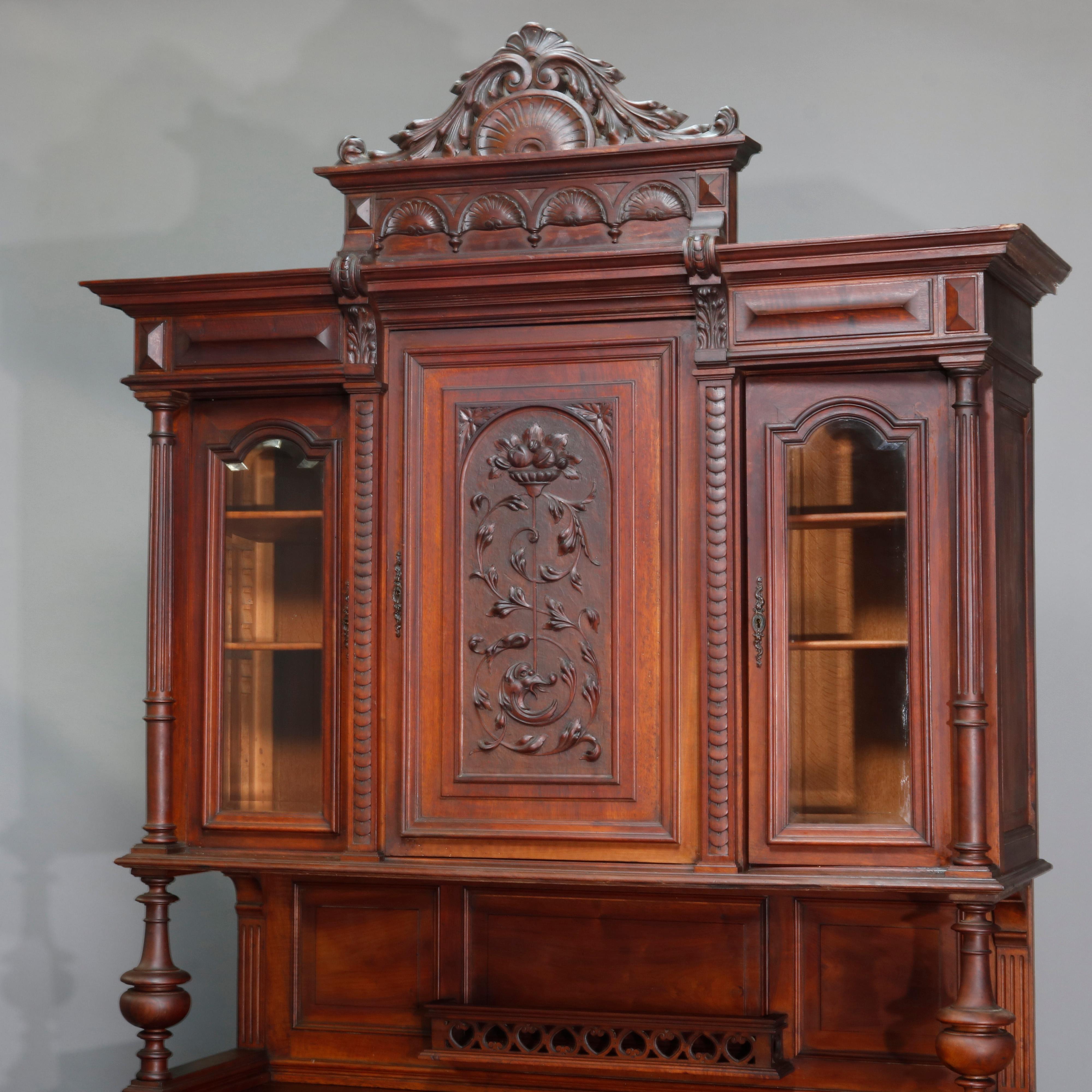 Antique oversized French Renaissance carved walnut cupboard with exaggerated crest having acanthus and shell, surmounting triple door cabinet with carved central panel with dolphin, foliate, scroll and fruit urn with flanking arched beveled glass