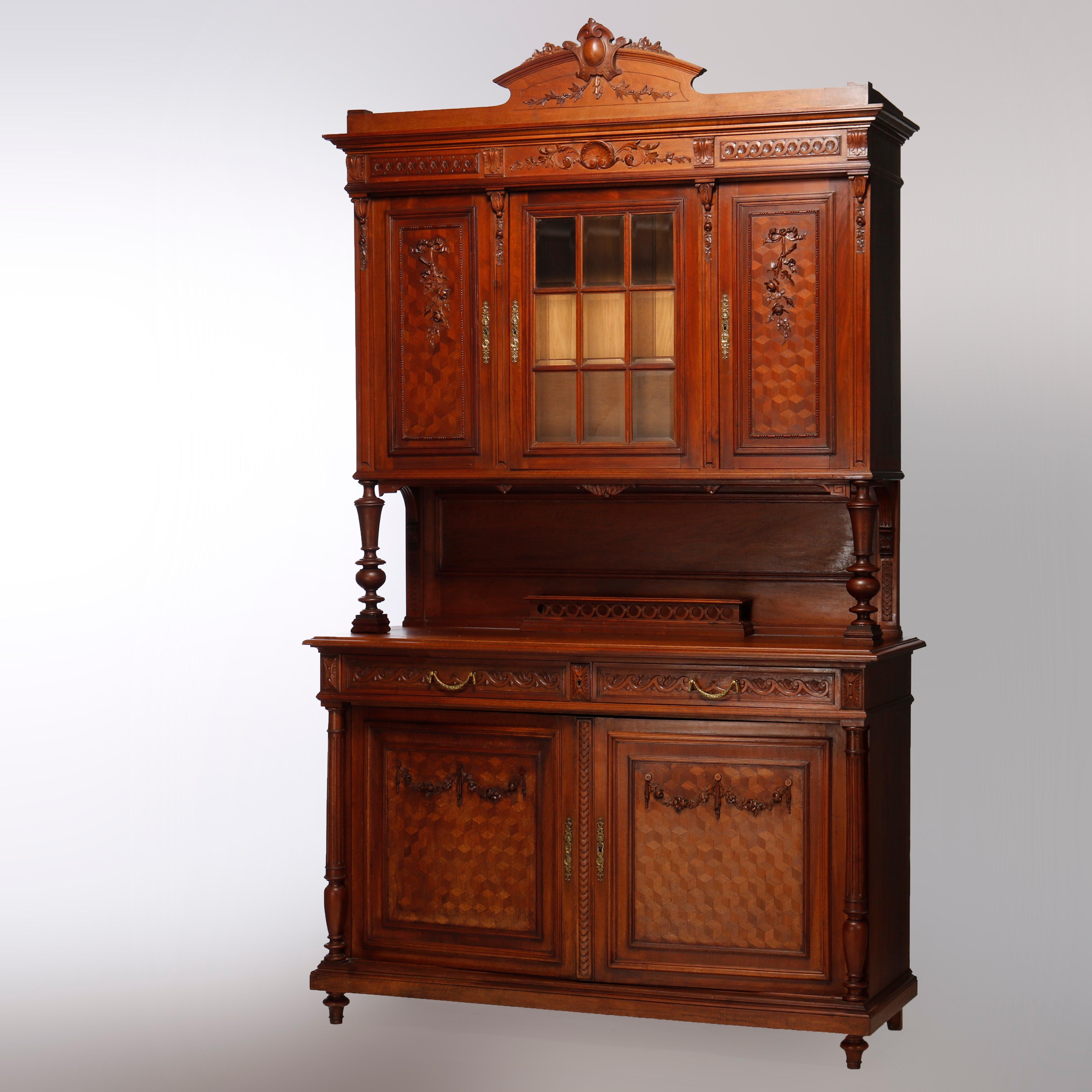 An antique French Renaissance court cupboard offers walnut construction with crest having central carved cartouche and flanking foliate elements over upper cabinet with central glass door with flaking parquetry blind doors with foliate mounts over