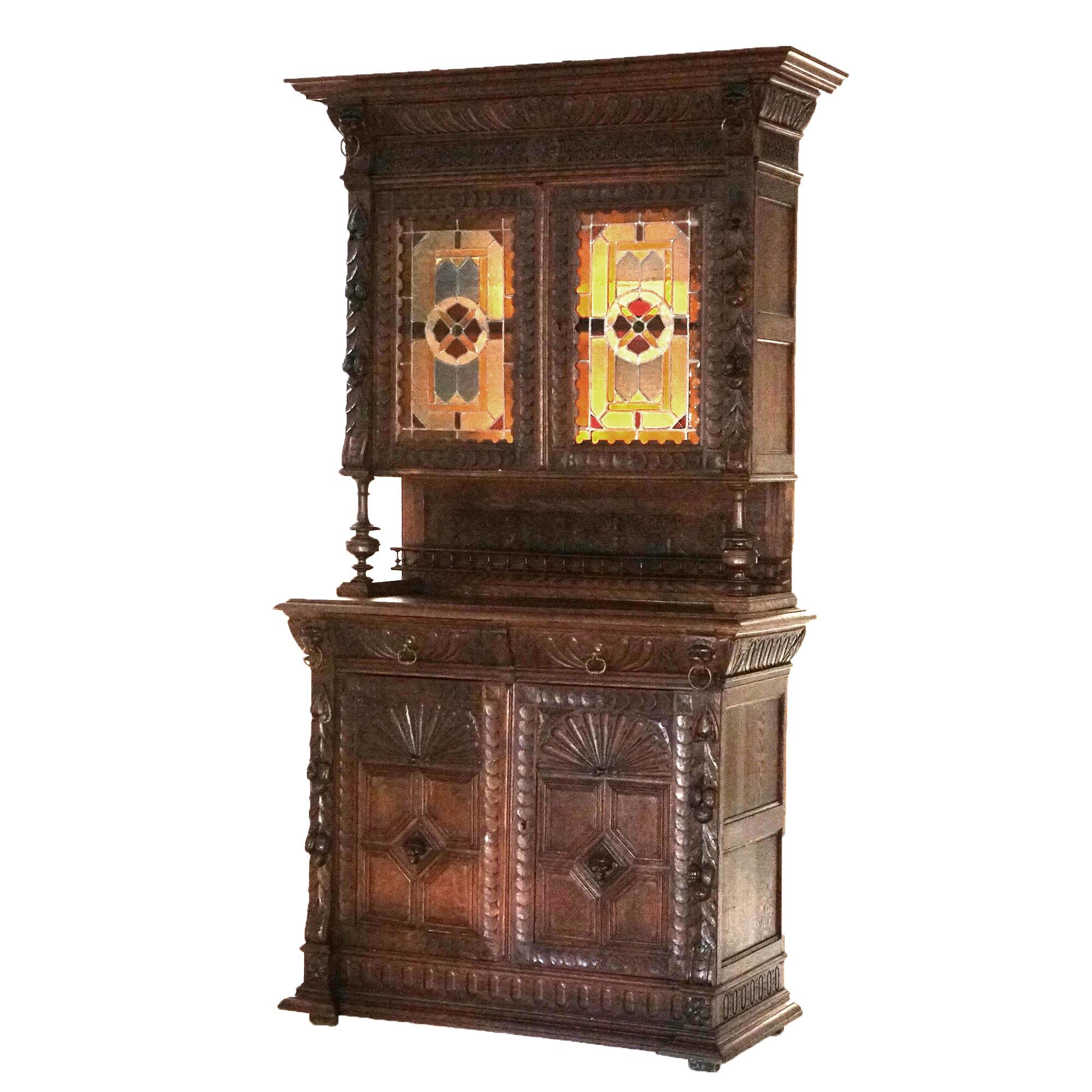 An antique French Renaissance figural sideboard offers deeply carved oak construction with upper having cabinet with leaded stained glass doors opening to shelved interior surmounting lower case with balustrade supports, two drawers and double door