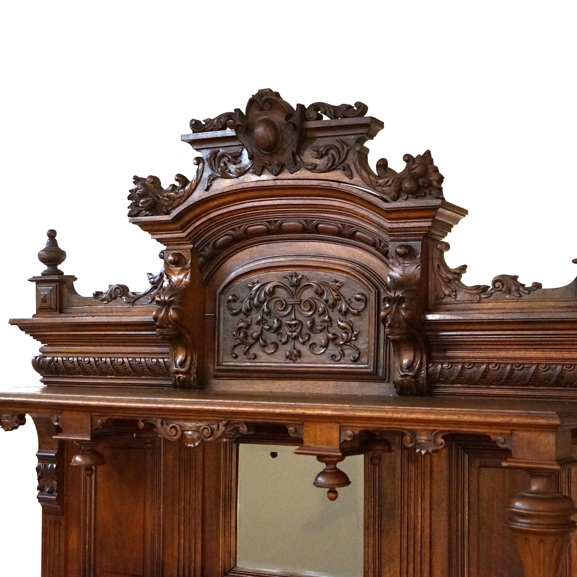 An antique figural French Renaissance hunt board server offers walnut construction with foliate carved pediment having central cartouche and flanking lion heads over backsplash with central beveled mirror and flanking urn form supports; lower marble