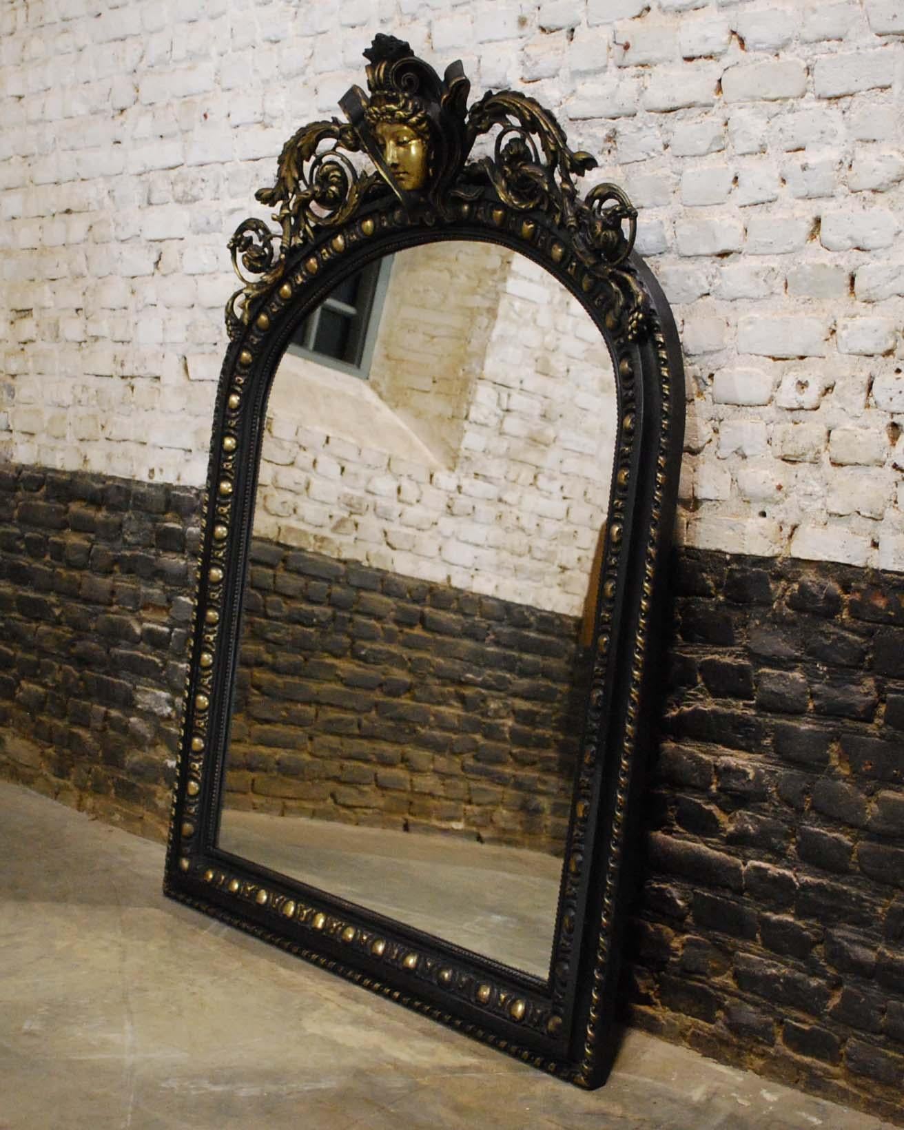 An antique French mirror made in the ancient European Renaissance style. 
The frame has a gadrooned edge and pearl beading surrounding the glass. The arched top is decorated with a central positioned serene women's head flanked by elegant